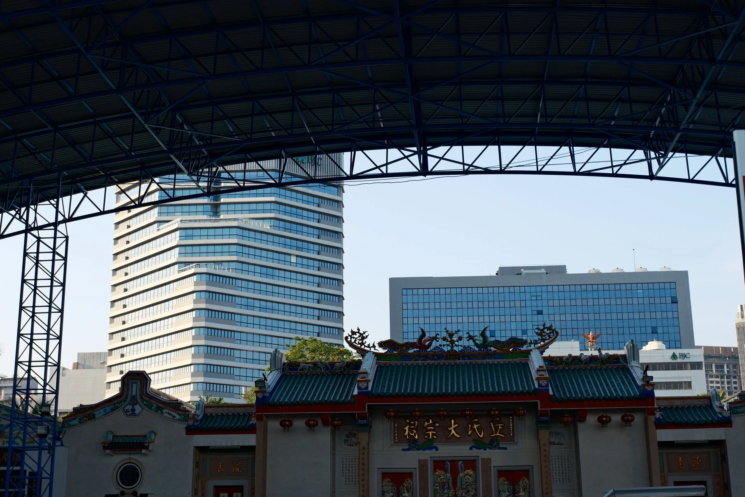 Cityscape view showing modern high-rise buildings behind a traditional Chinese temple with ornate decorations and a green tiled roof.