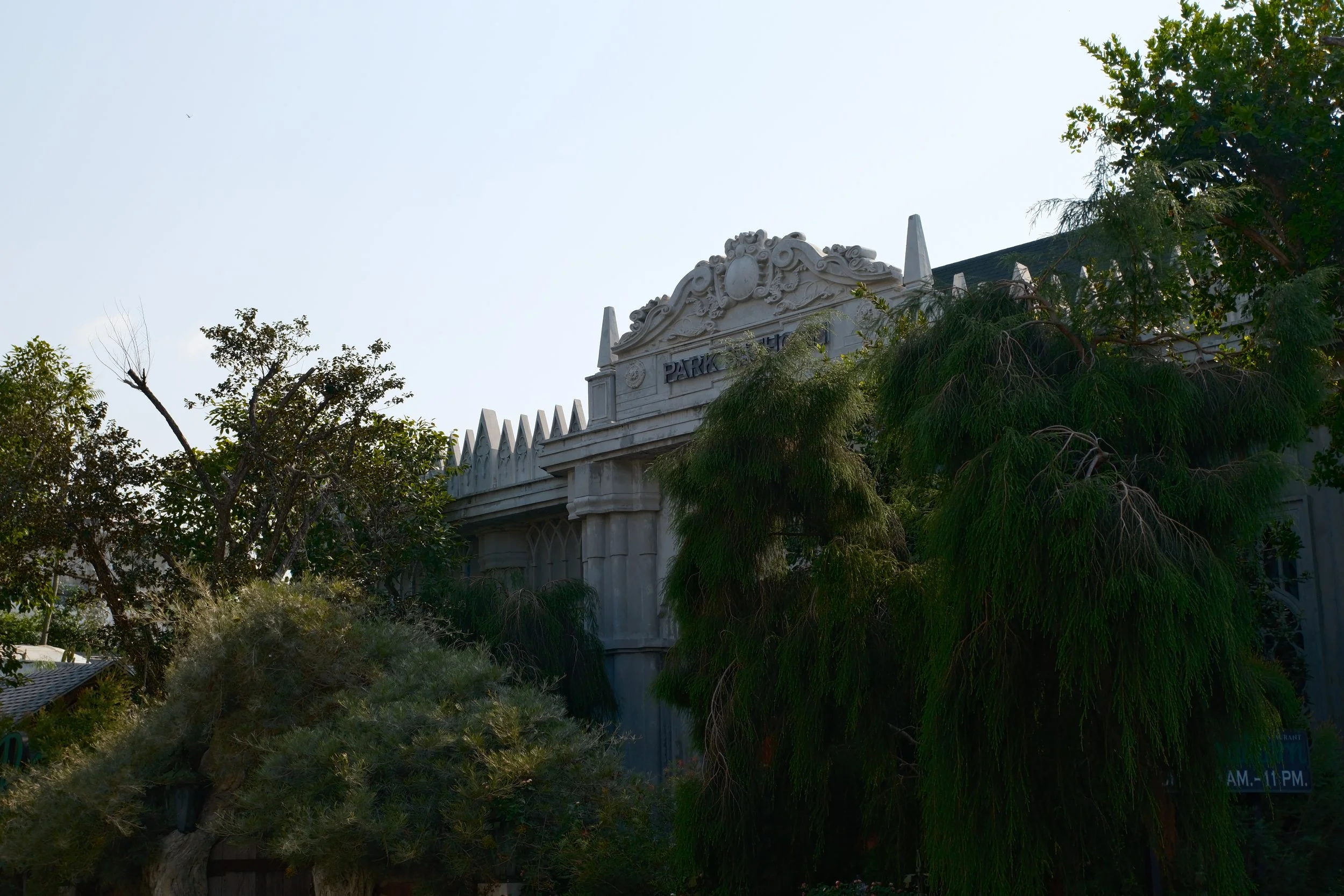 A historic building with ornate architectural details partly obscured by trees and greenery.