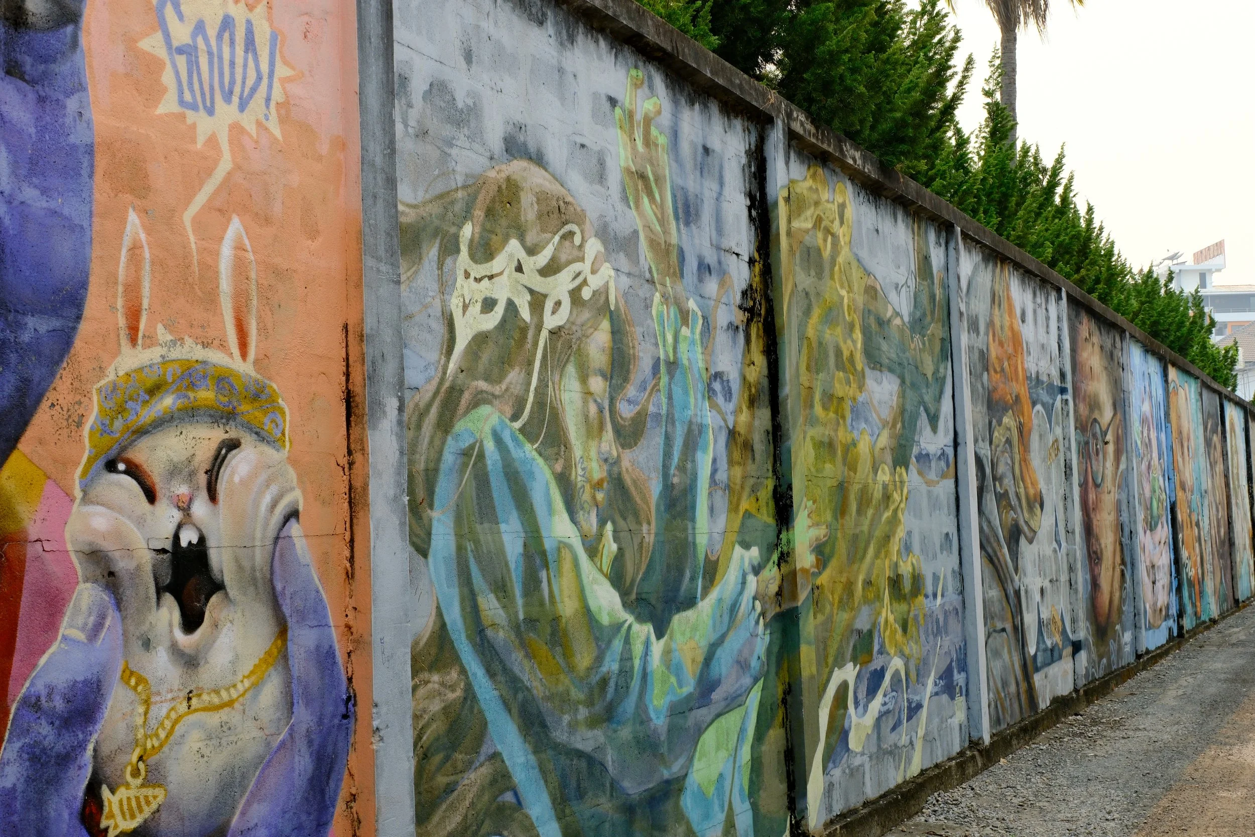 A colorful mural painted on a long concrete wall features various animals and abstract figures, including a rabbit wearing a bandana with a yellow chain, and multiple other stylized animals and shapes in shades of blue, green, yellow, and orange.