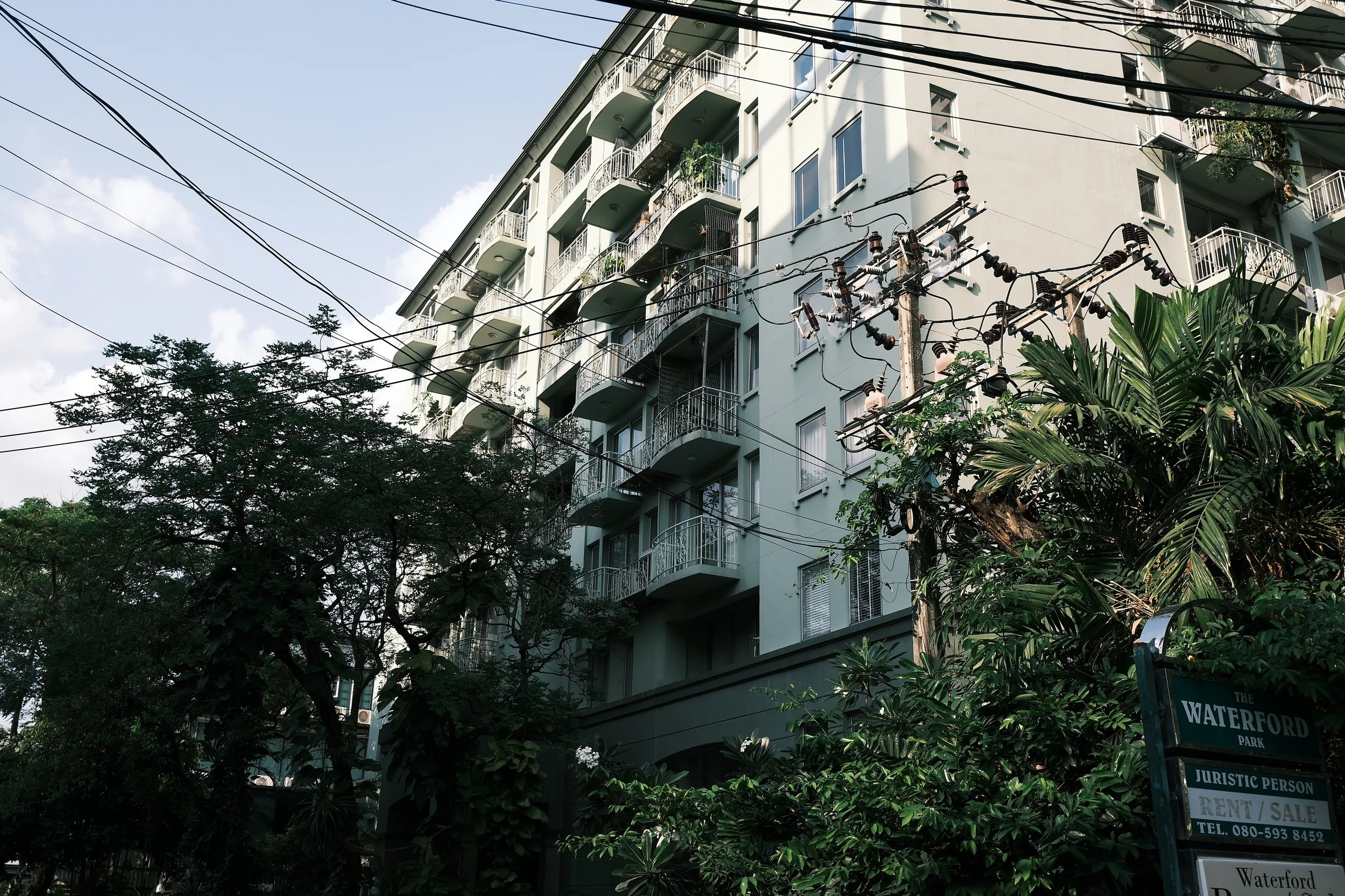 Multi-story residential building with balconies, surrounded by trees and electrical wires, with a sign indicating it's in Waterford Park.