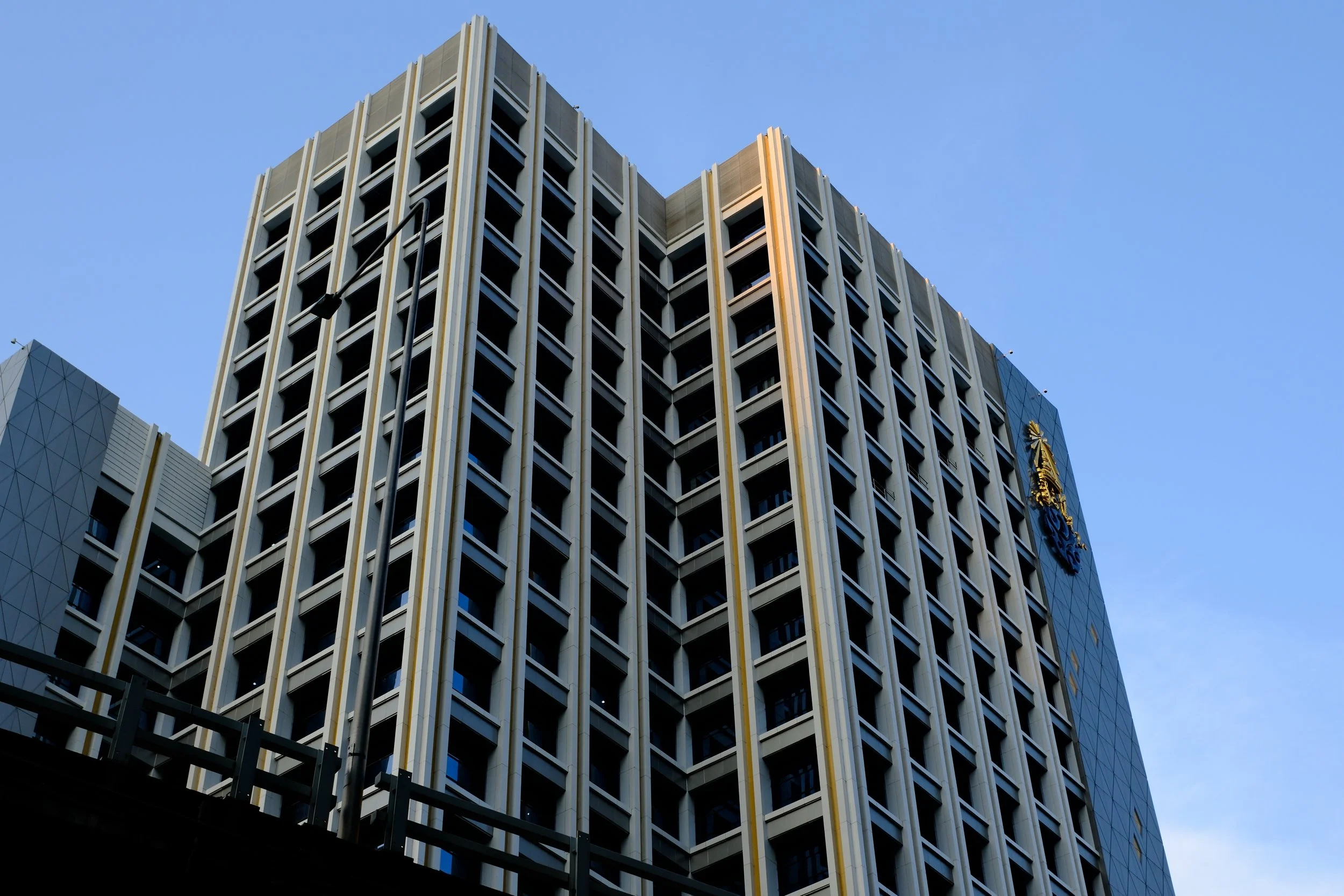A tall modern office building with vertical beige and black accents and a crest on the side, against a clear blue sky.
