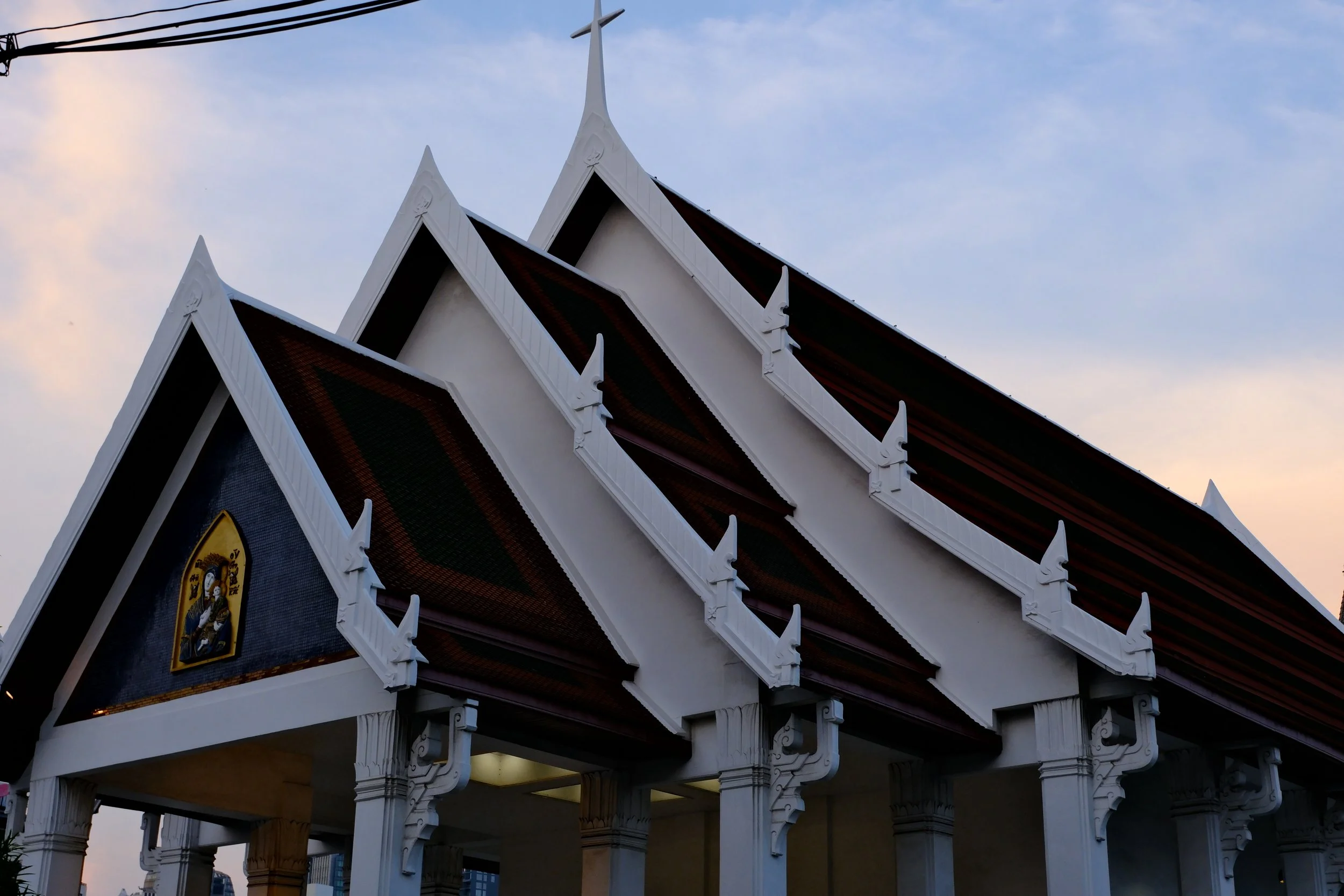Traditional Thai temple with ornate multi-tiered roof against a cloudy sky at dusk