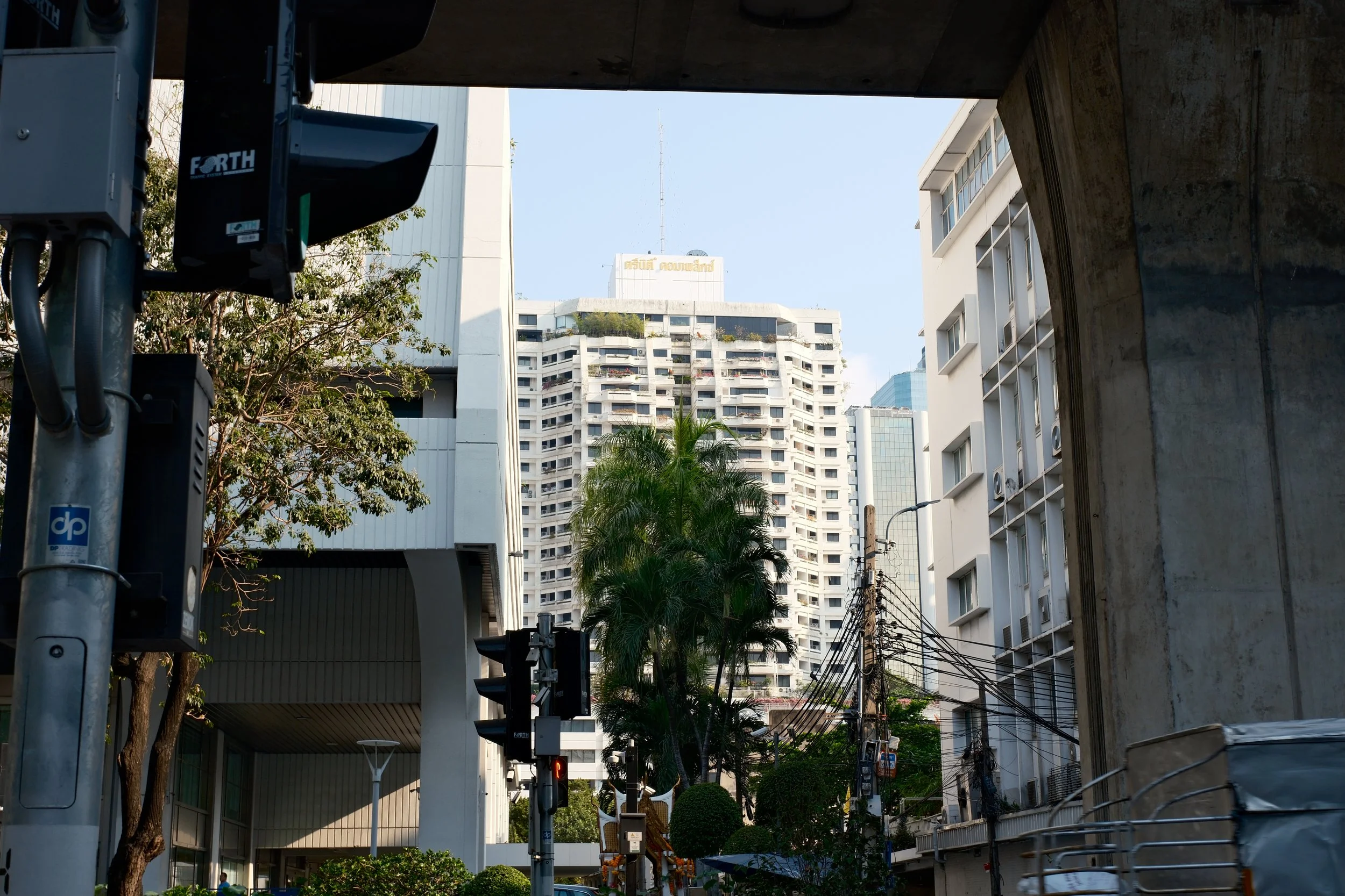 City street scene with tall apartment buildings, trees, utility poles and wires, traffic lights, and a modern building frame.