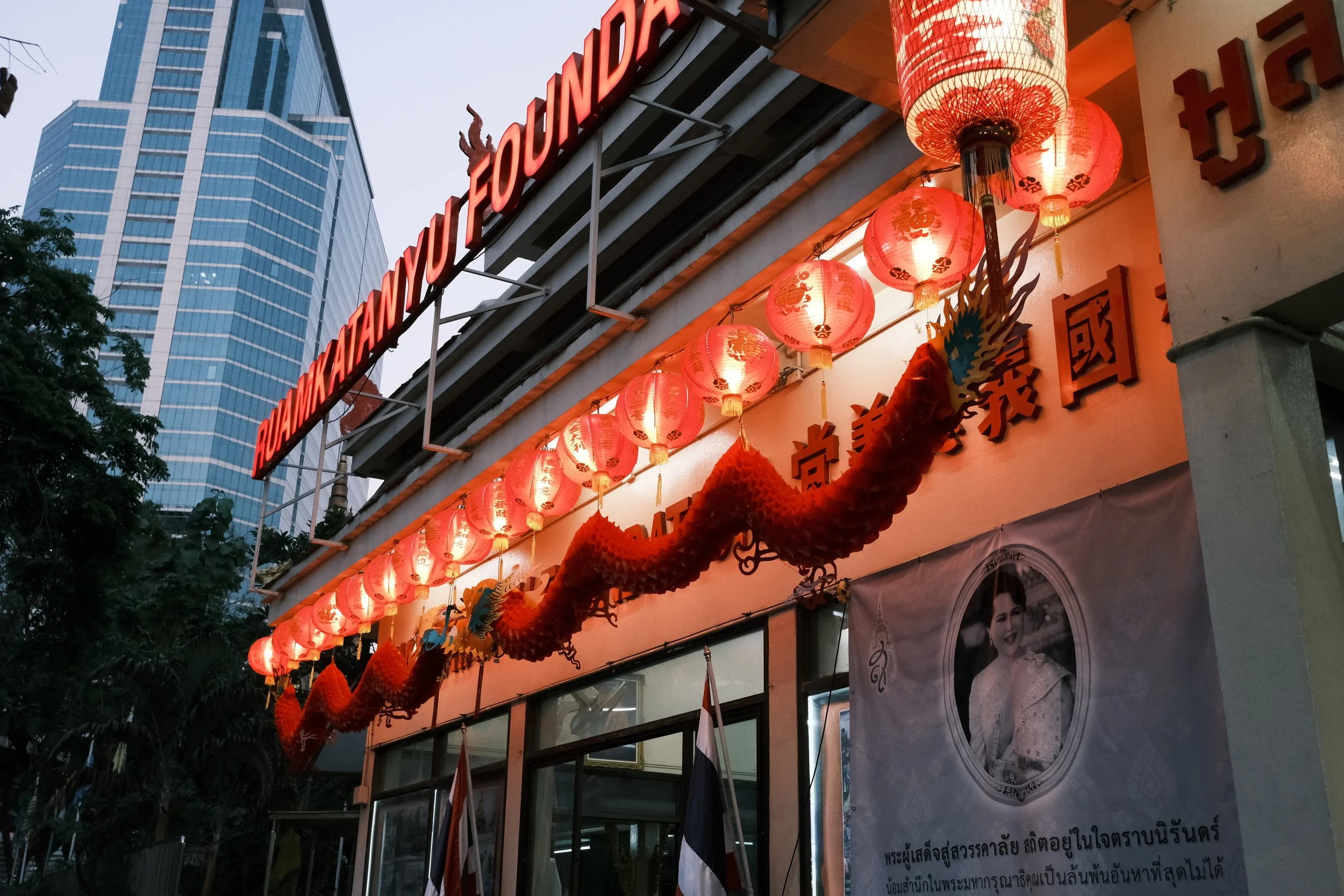 Exterior view of the Bukit-Myanmar restaurant adorned with red lanterns and a decorative dragon banner, with a modern skyscraper in the background.