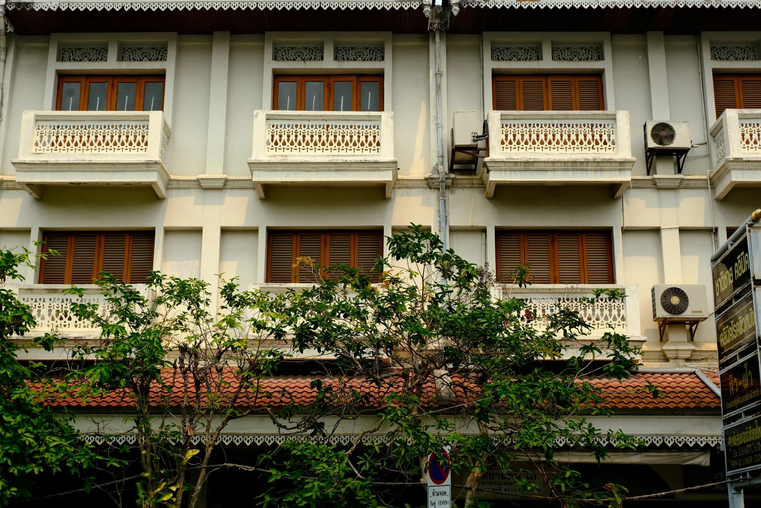 Multi-story building with white exterior, wooden window shutters, decorative balcony railings, and visible air conditioning units.