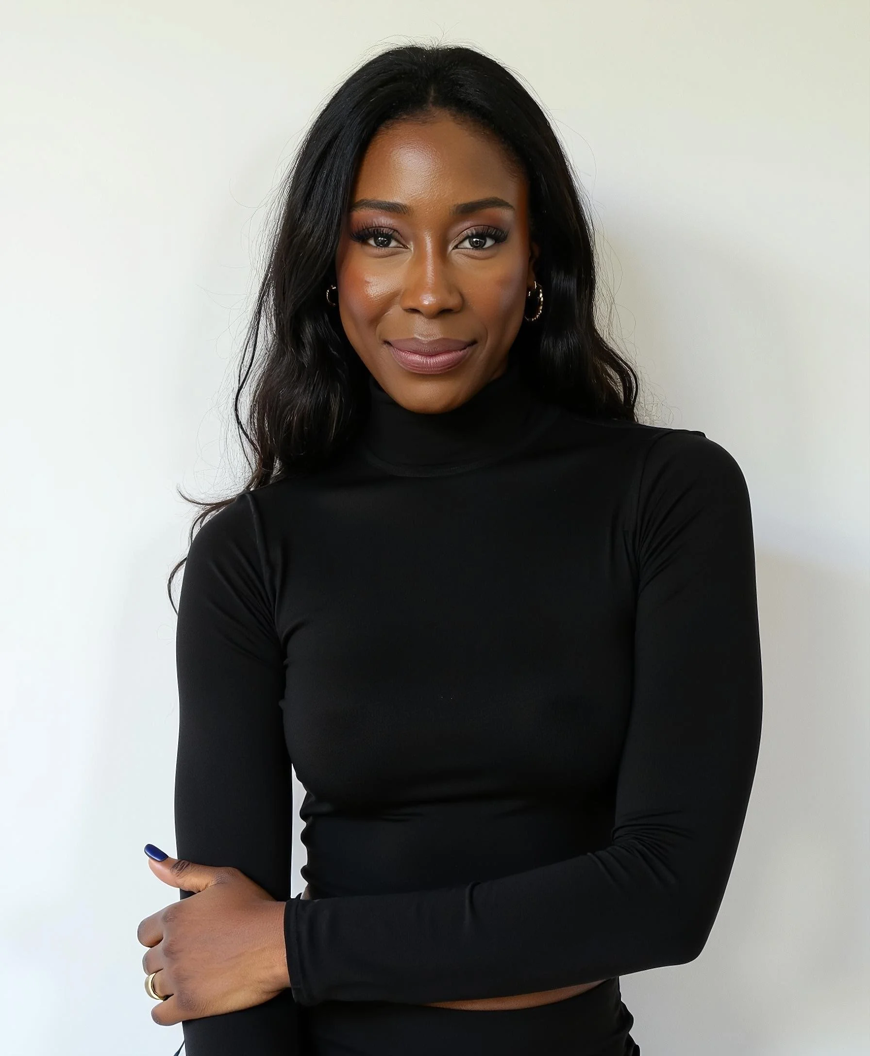 A woman with long black hair, wearing a black turtleneck top, standing against a plain white background, smiling softly.