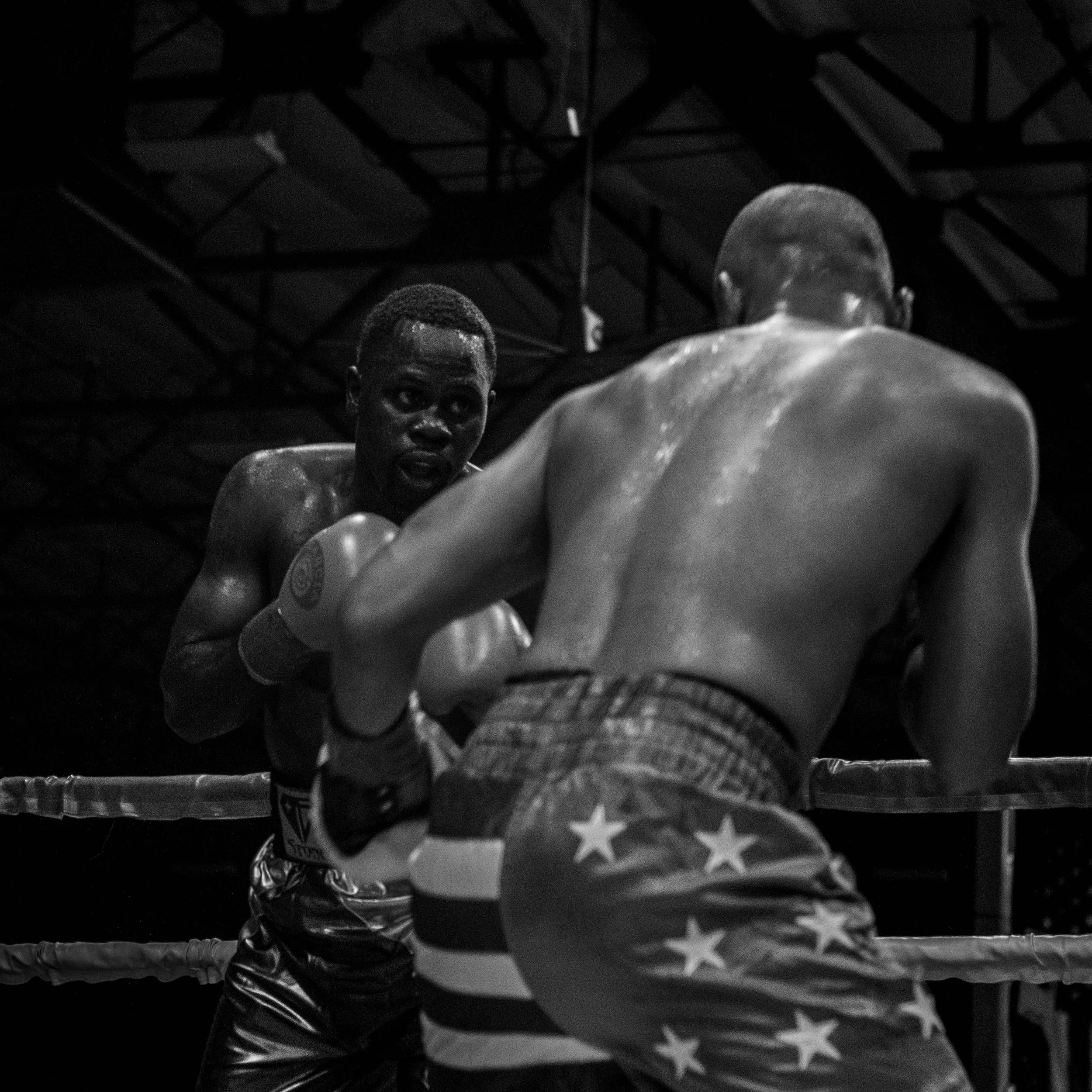 Two boxers in an intense boxing match inside a ring, with one boxer throwing a punch at the other, both sweating and focused.