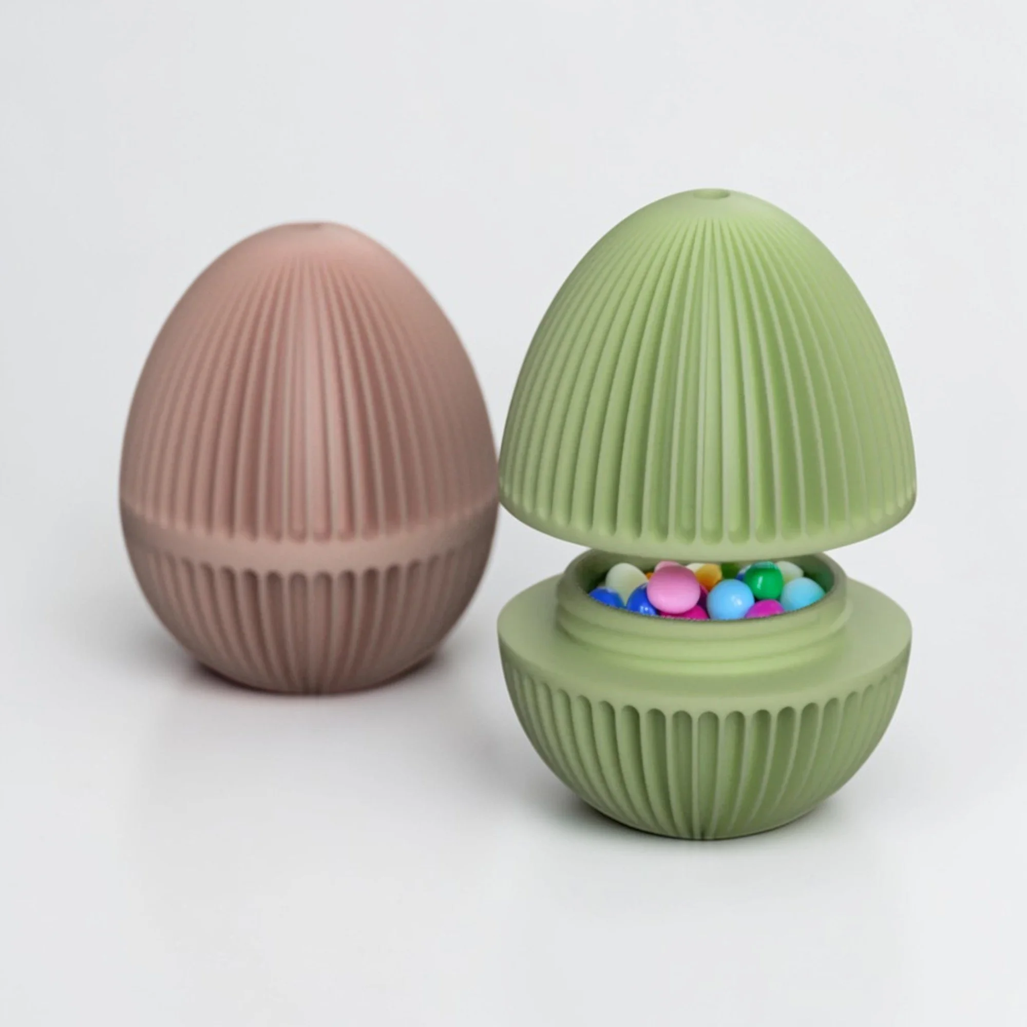 Osterei zum Befüllen in Hellgrün, geöffnet mit bunten kleinen Eiern im Inneren, daneben eine geschlossene Variante in zartem Rosa.