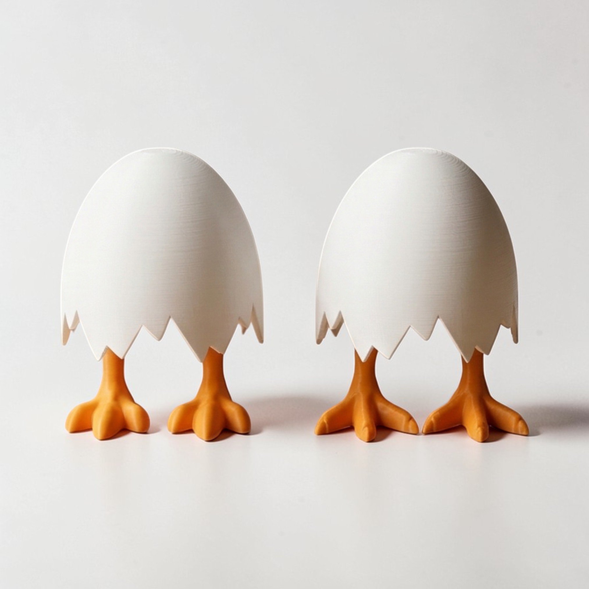 Zwei weiße Eierfiguren mit orangefarbenen Beinen nebeneinander, humorvolle Osterdeko im minimalistischen Design auf hellem Hintergrund.