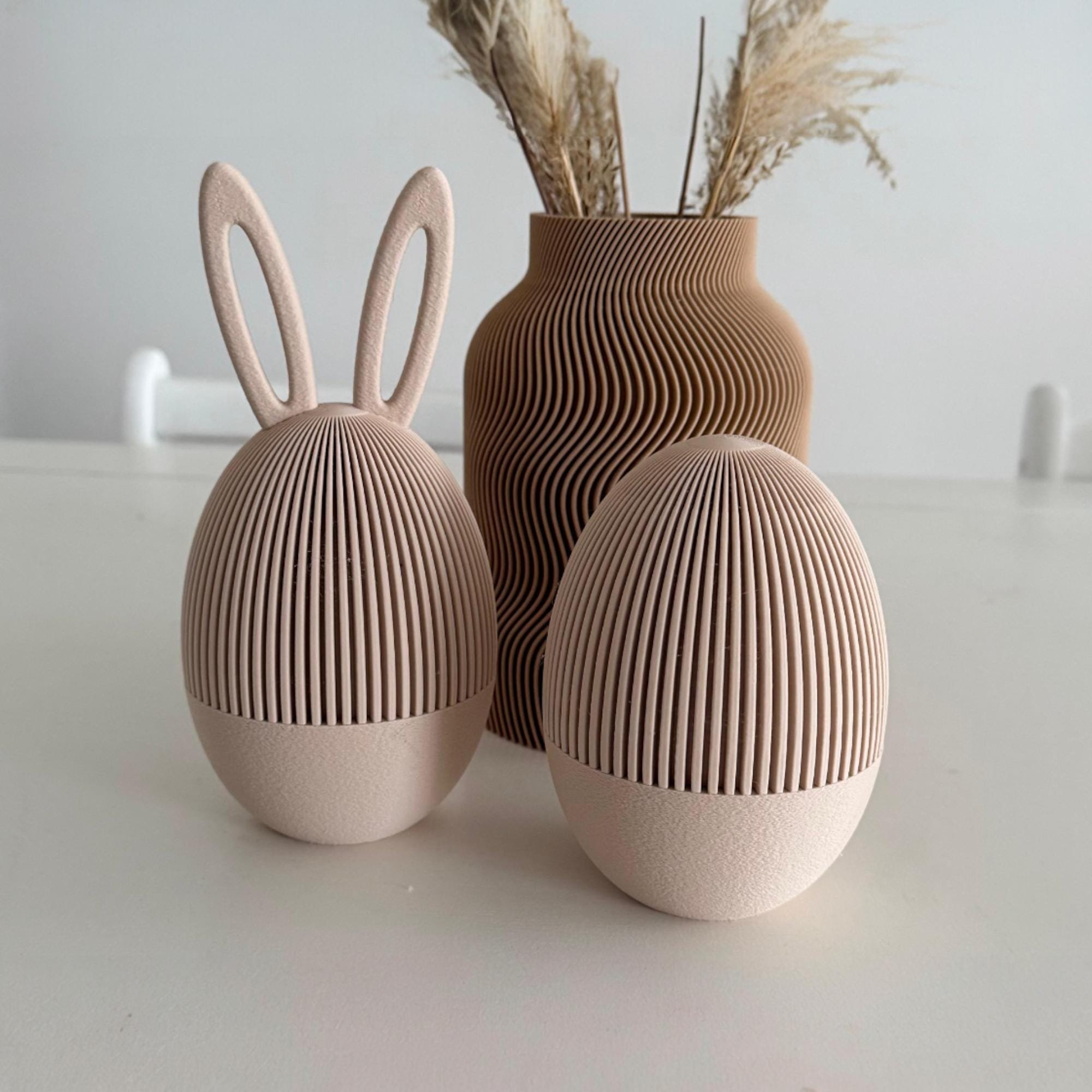 Befüllbare Osterei Dosen in dunkler zweifarbiger Variante auf hellem Regal mit Vase und Trockenblumen als stilvolle Japandi Osterdekoration.