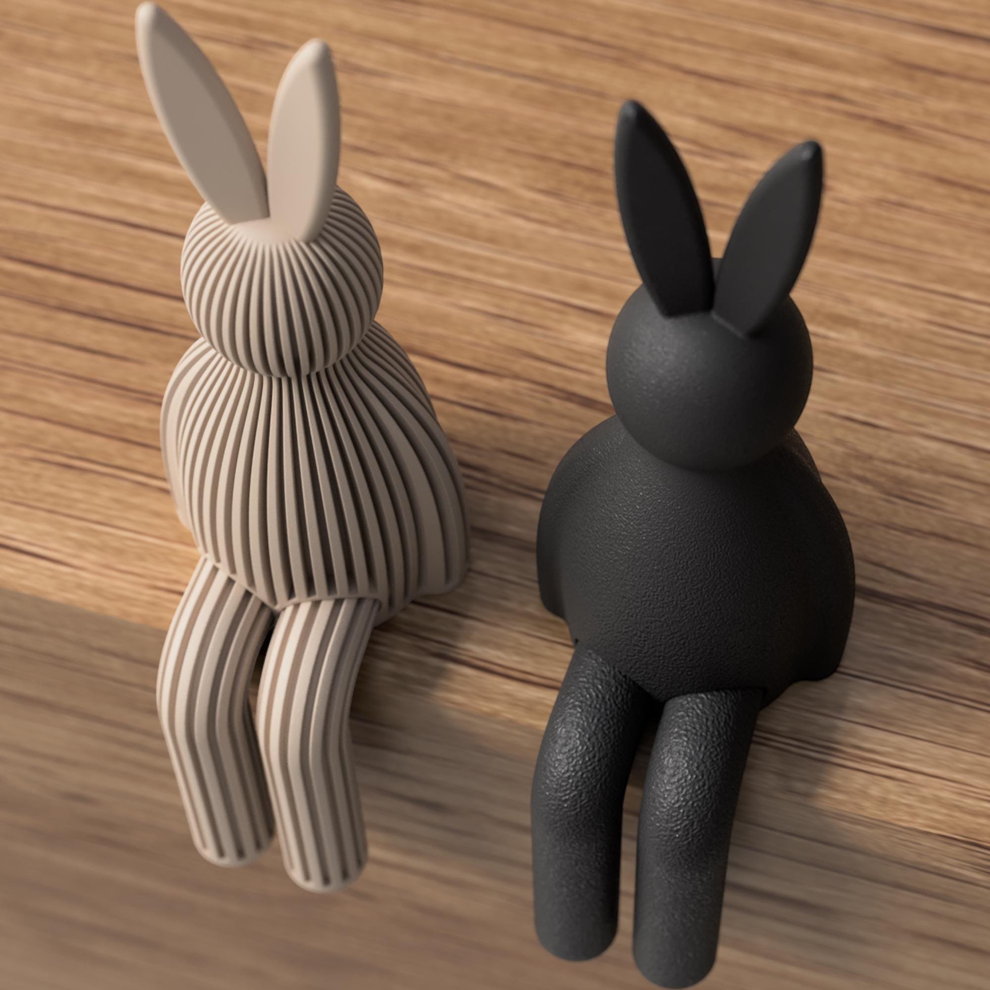 Sitzender Japandi Osterhase in Taupe und Schwarz als Farbvergleich, links gerippt und rechts glatt, mit hängenden Beinen auf Holzoberfläche.