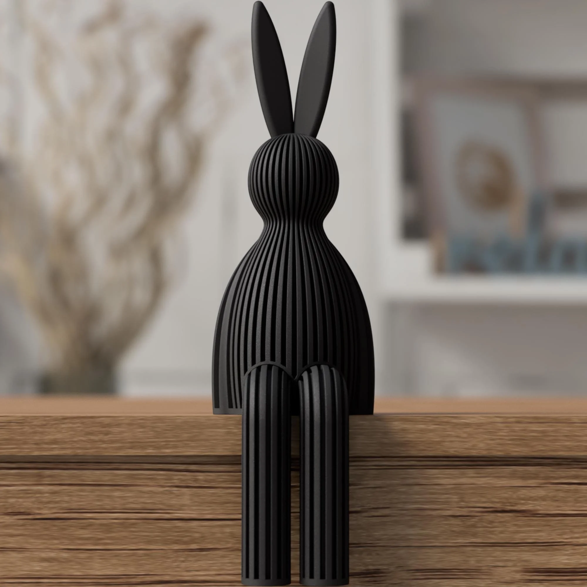 Schwarzer Japandi Osterhase mit gerippter Oberfläche, sitzend auf einer Holzkante mit hängenden Beinen vor unscharfem Wohnhintergrund.