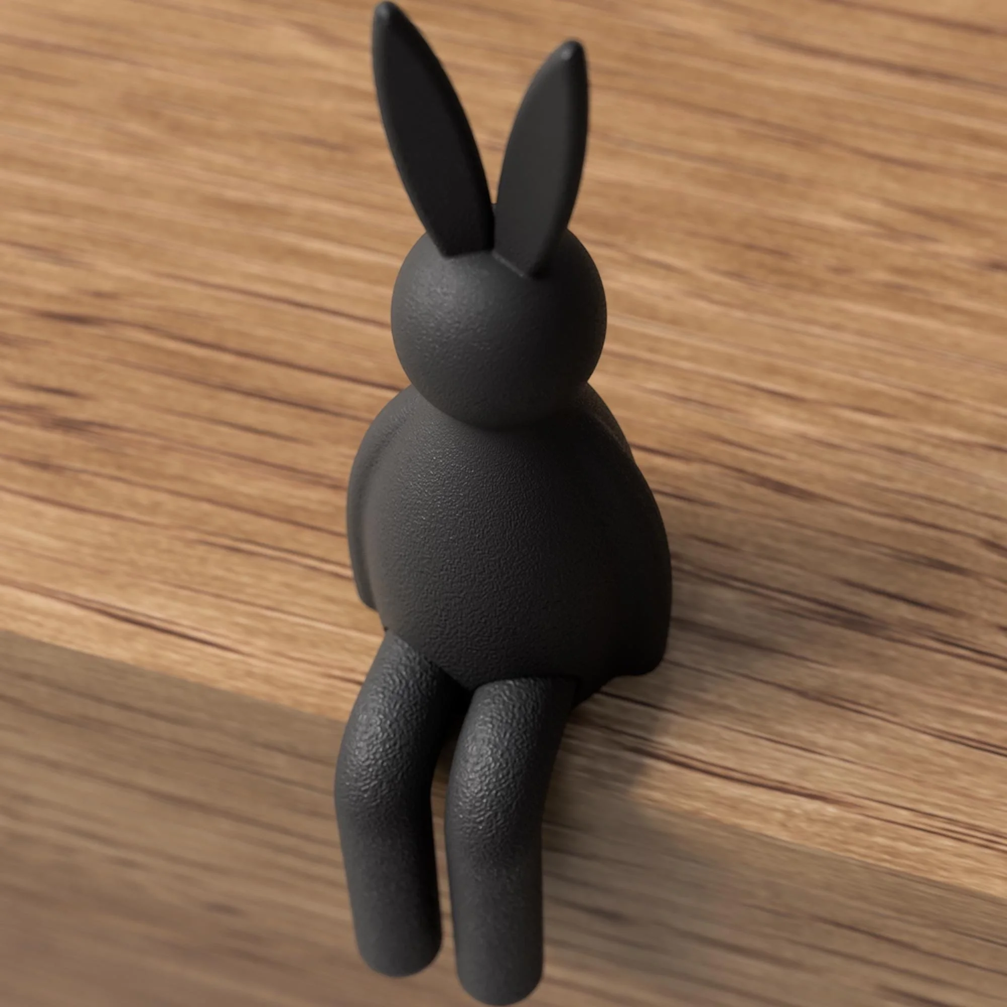 Schwarzer Osterhase mit glatter, matter Oberfläche als sitzende Dekofigur auf Holz mit klarer Form und hängenden Beinen.