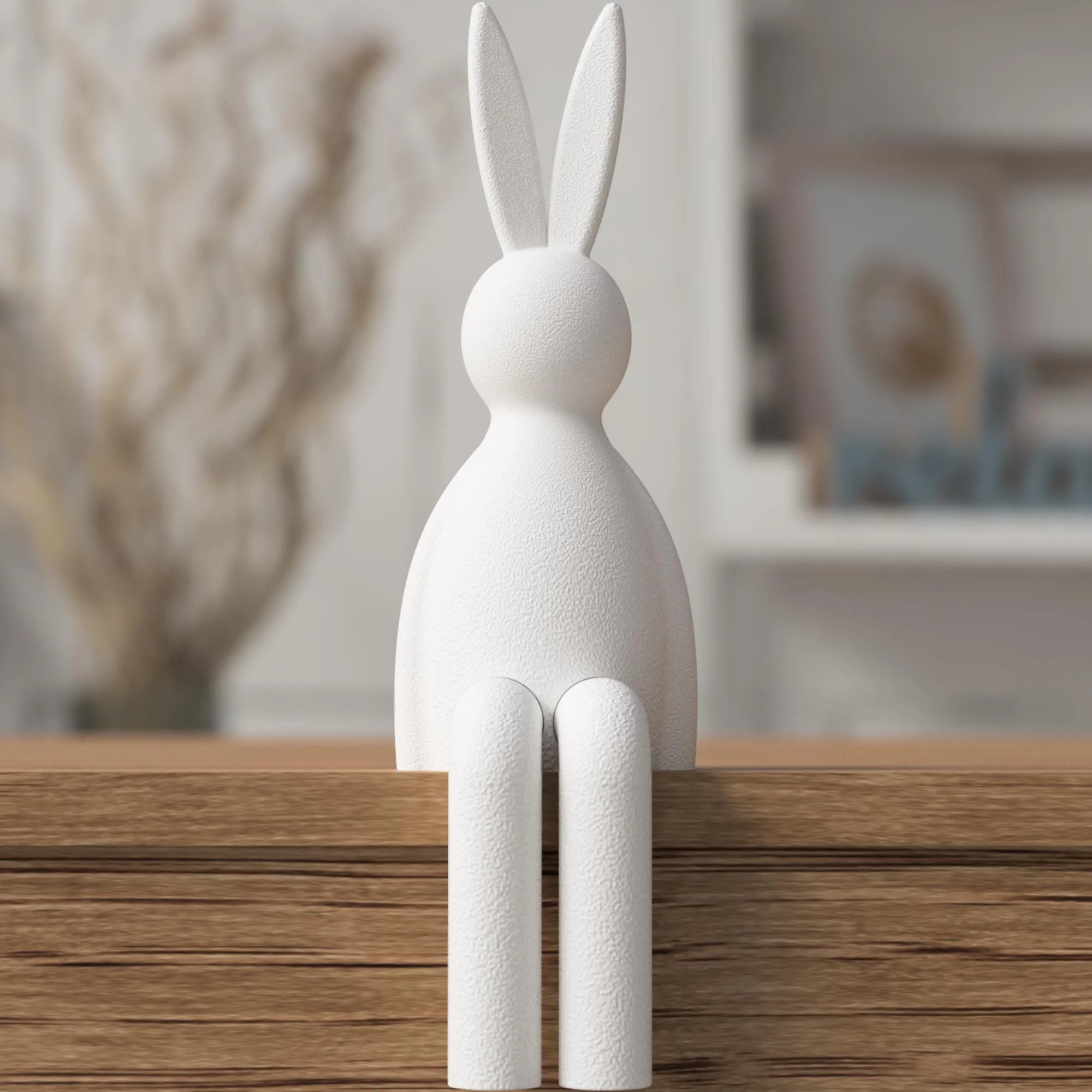 Weiße Osterfigur mit glatter Oberfläche, sitzend auf einer Holzkante vor sanft unscharfem Hintergrund mit langen Ohren und hängenden Beinen.