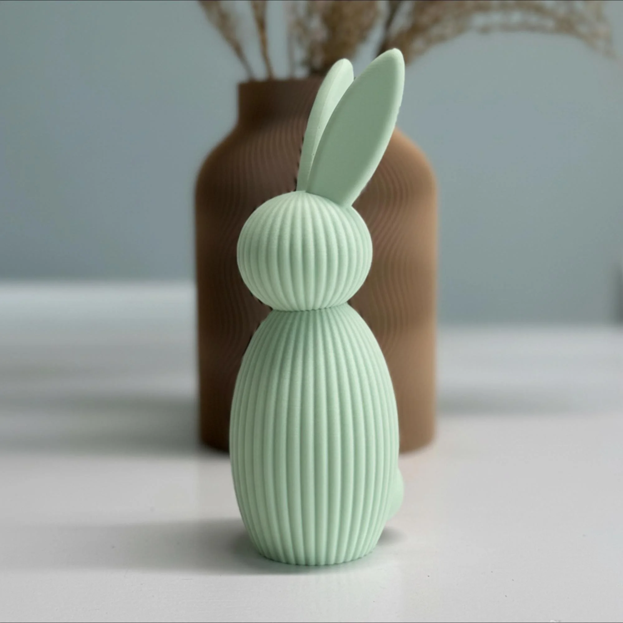 Mintgrüner Deko-Hase aus PLA im 3D-Druck auf hellem Untergrund, leicht seitlich inszeniert vor schlichter Vase im skandinavischen Wohnstil.