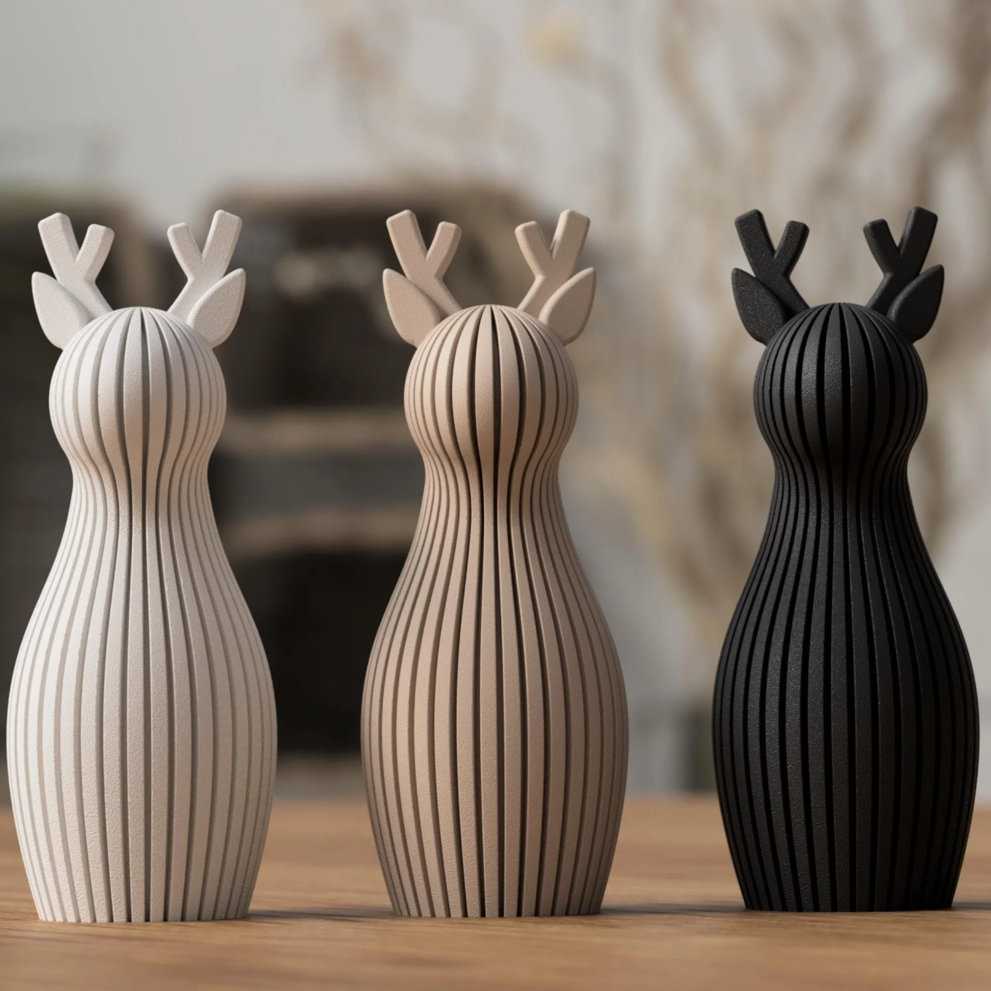 Drei minimalistische Rentier Figuren in Weiß, Beige und Schwarz, nebeneinander auf Holz arrangiert als ruhiges Deko-Ensemble.