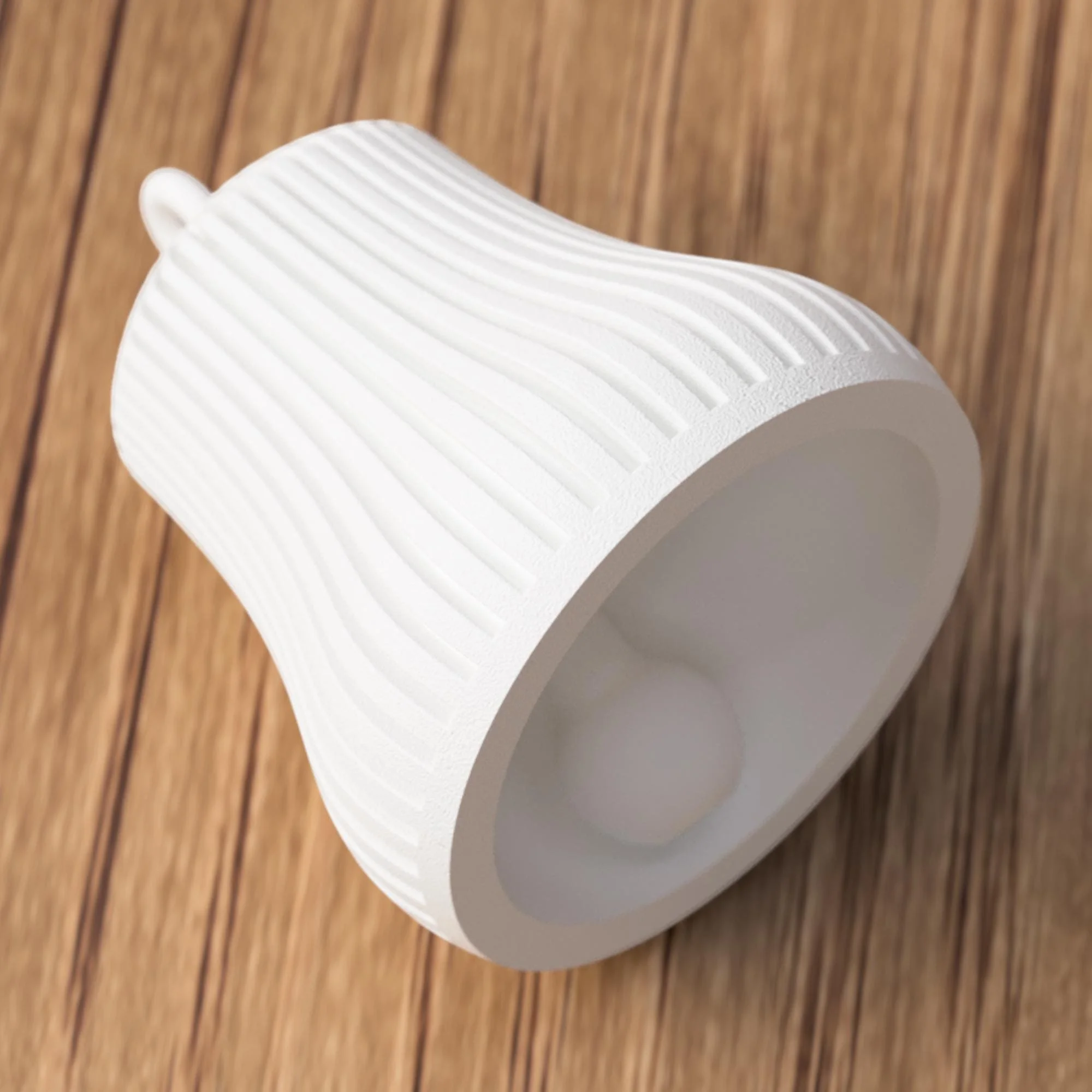 Weiße Glocke liegend mit sichtbarem Klöppel im Inneren, zeigt Form, Material und präzise Verarbeitung im Detail