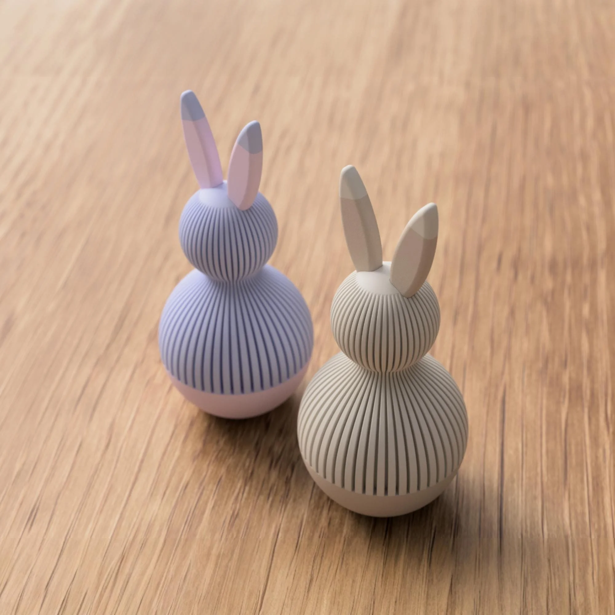 Zwei zweifarbige Osterhasen in Lavendel und Beige aus leicht erhöhter Perspektive, schlicht gestaltet mit feiner Rillenstruktur auf Holz.