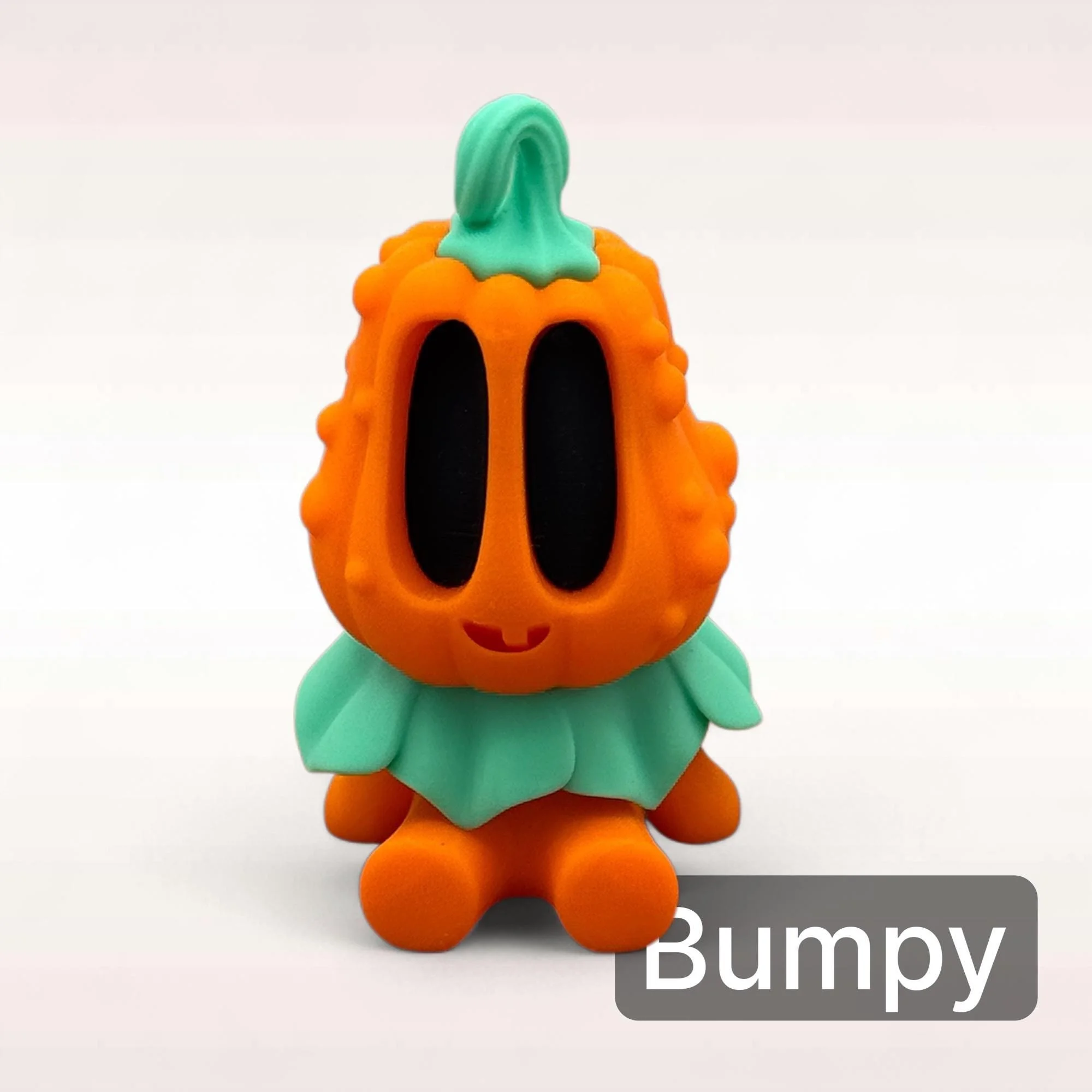 Mini Kürbis Figur Bumpy in Orange mit schwarzem Gesicht und grünem Blätterkragen als kompakte Herbst und Halloween Deko.