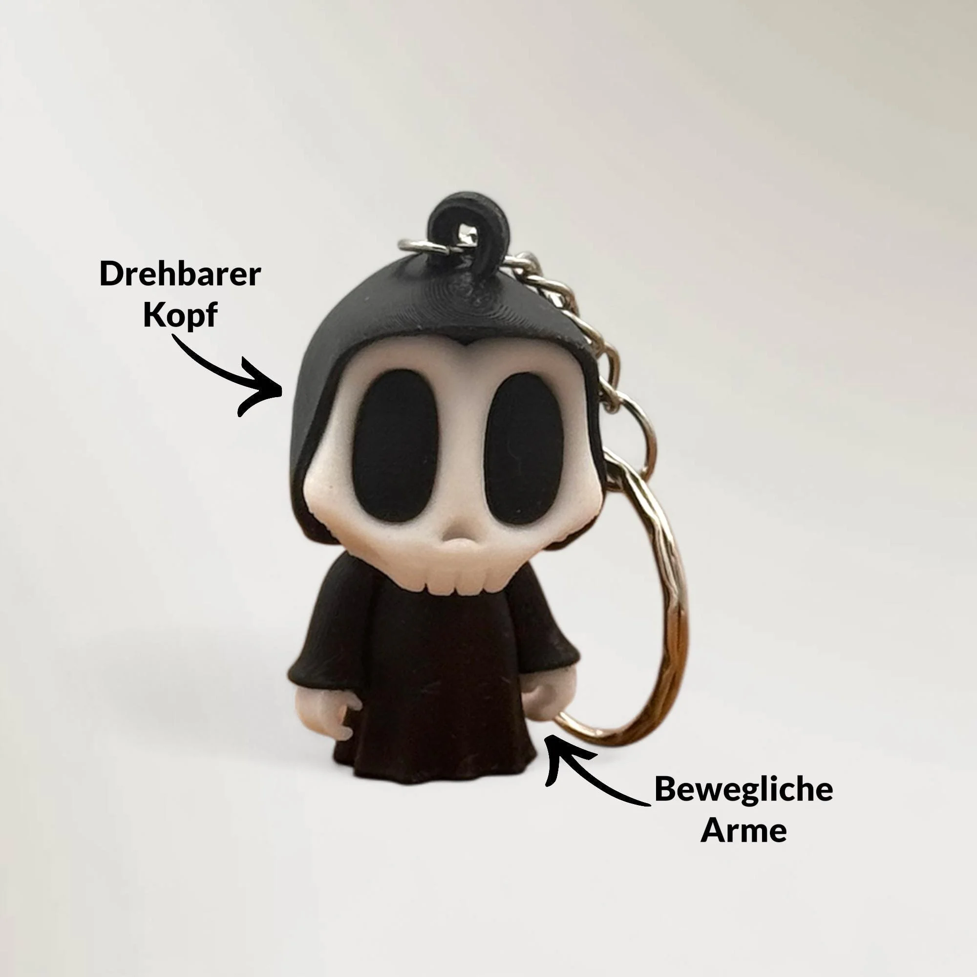 Schwarzer Skelett Schlüsselanhänger mit Metallring vor hellem Hintergrund, mit Pfeilen zu drehbarem Kopf und beweglichen Armen.