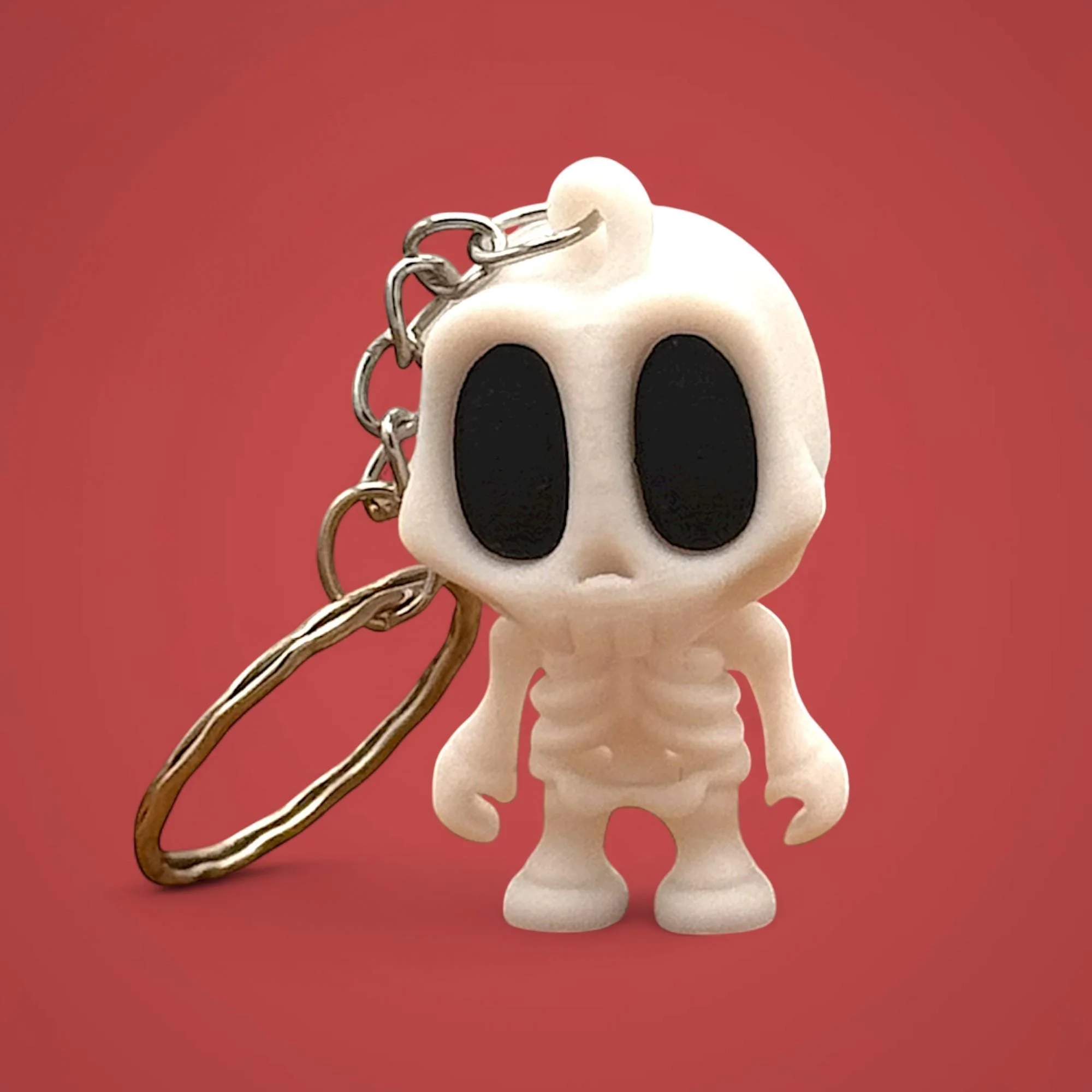 Weißer Skelett Schlüsselanhänger mit Metallring vor rotem Hintergrund.