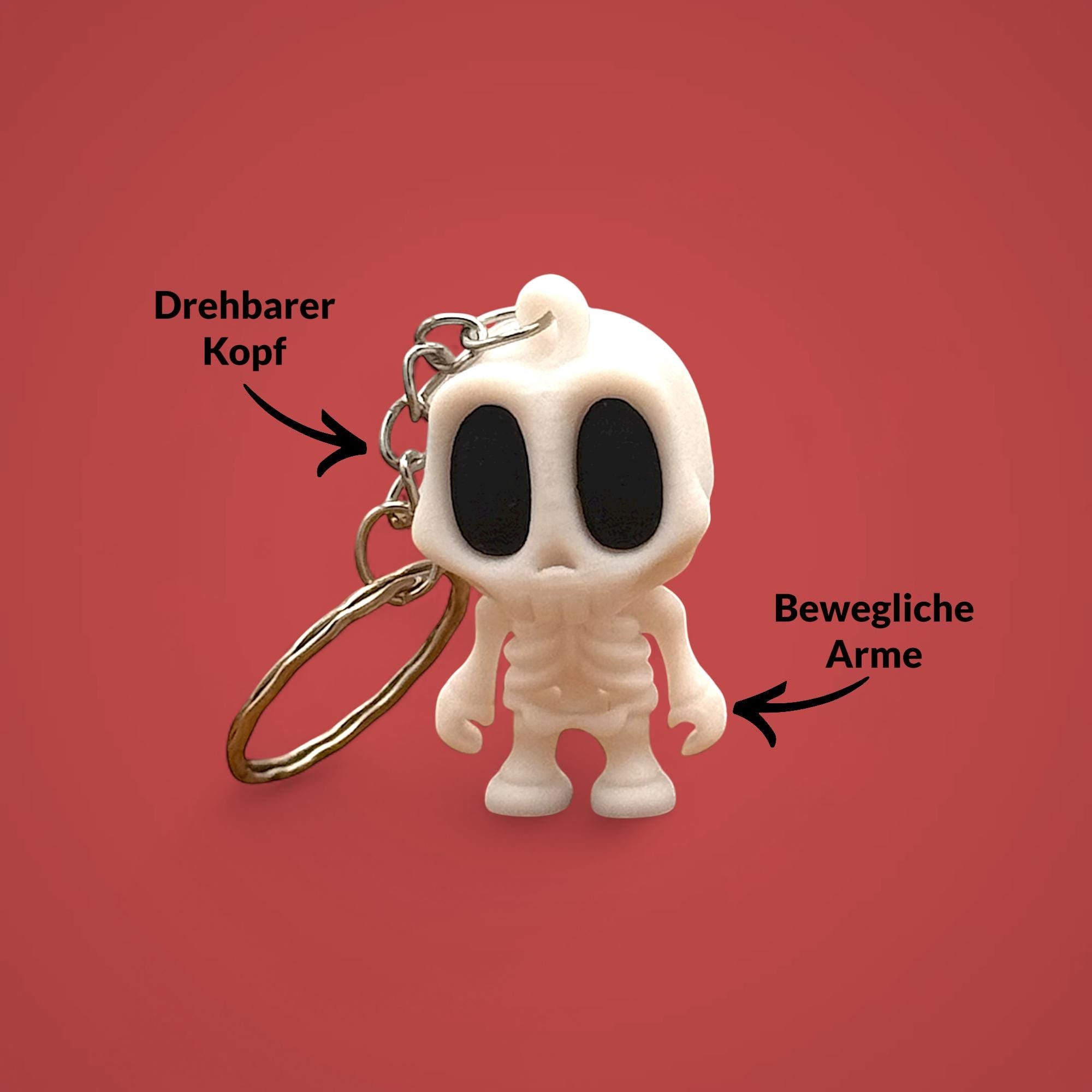 Weißer Skelett Schlüsselanhänger mit Metallring vor rotem Hintergrund, mit Pfeilen zu drehbarem Kopf und beweglichen Armen.
