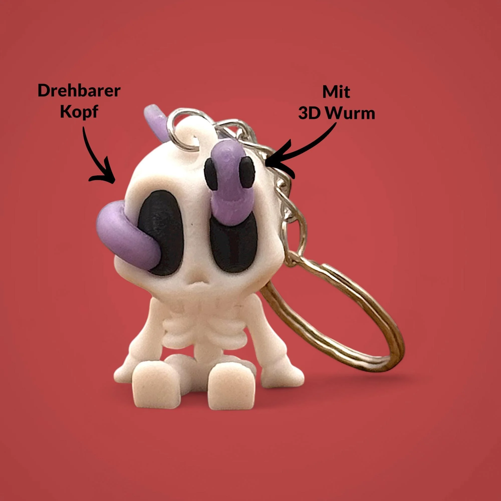 Sitzender Skelett Schlüsselanhänger mit lila Wurm auf dem Kopf und Metallring vor rotem Hintergrund, mit Pfeilen zu drehbarem Kopf und 3D Wurm.