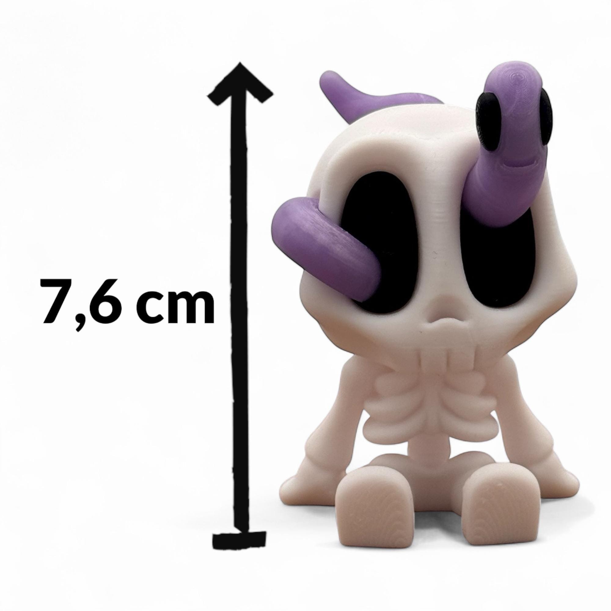Sitzendes weißes Mini-Skelett mit lila Wurm auf dem Kopf vor weißem Hintergrund. Links daneben zeigt ein schwarzer Pfeil die Höhe von 7,6 cm. Die Figur ist frontal sichtbar.