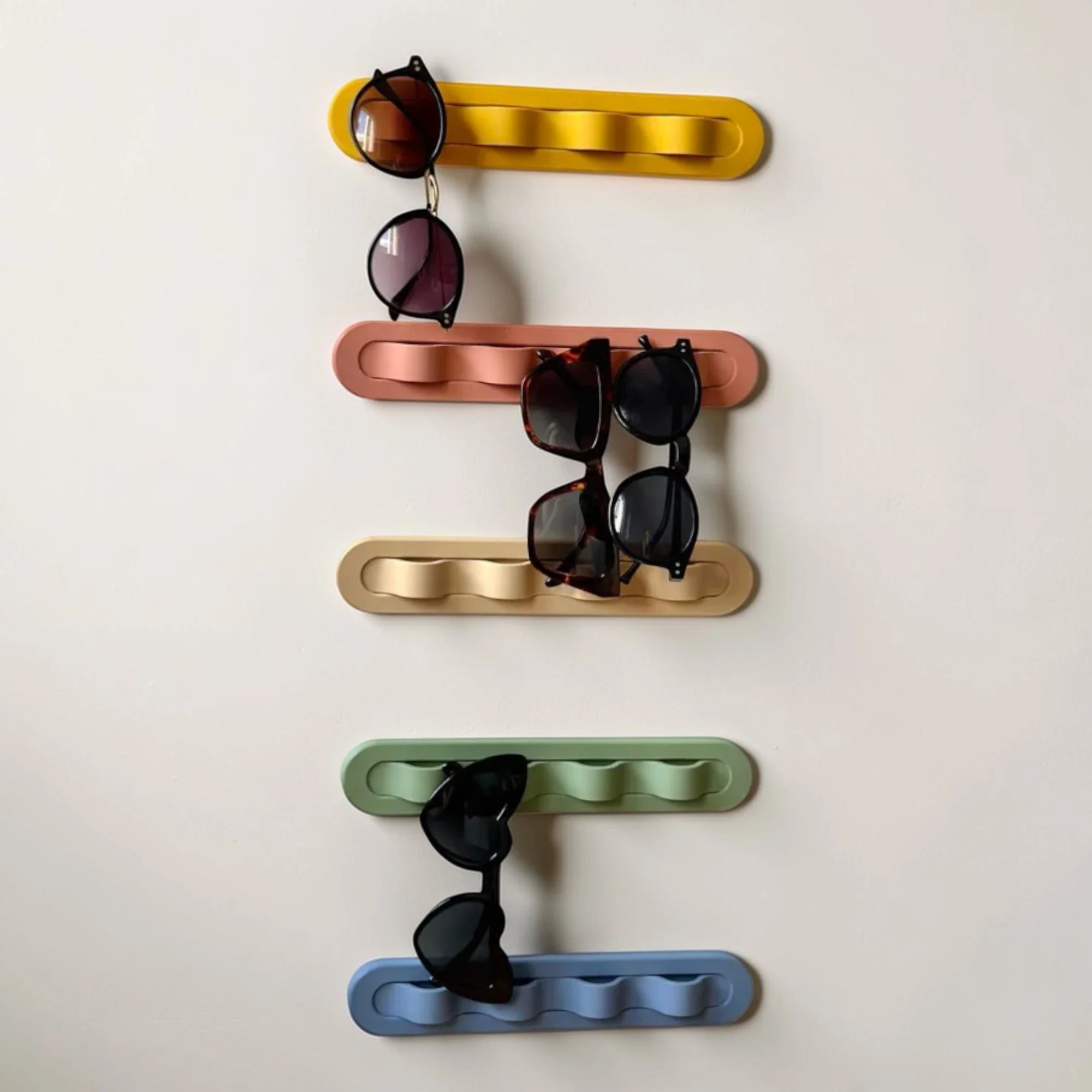 Sonnenbrillenhalter für die Wand in mehreren Farbvarianten mit vier eingehängten Brillen, dekorativ und griffbereit im klaren modernen Design.