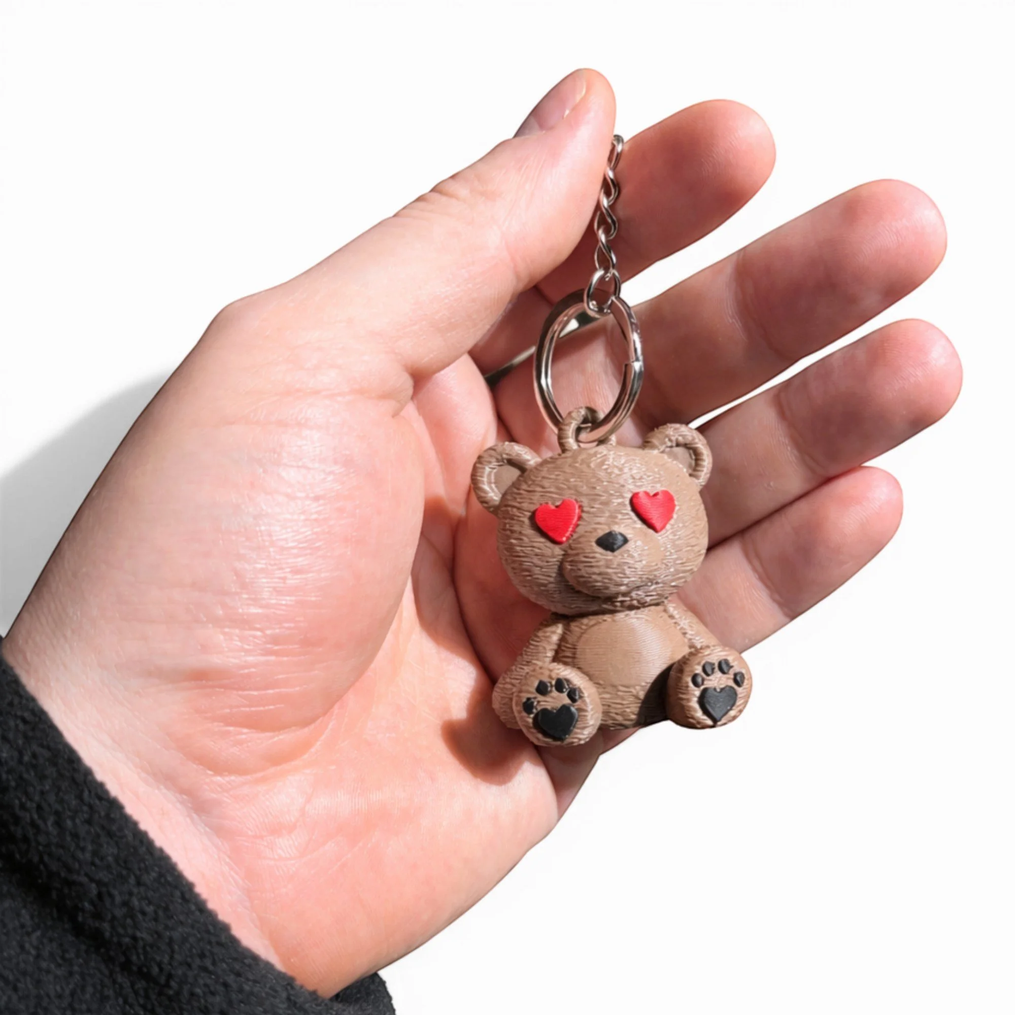 Brauner Teddy Schlüsselanhänger mit Herzaugen in einer Hand, kompakt und detailreich mit Metallkette für Schlüsselbund, Tasche oder Rucksack.