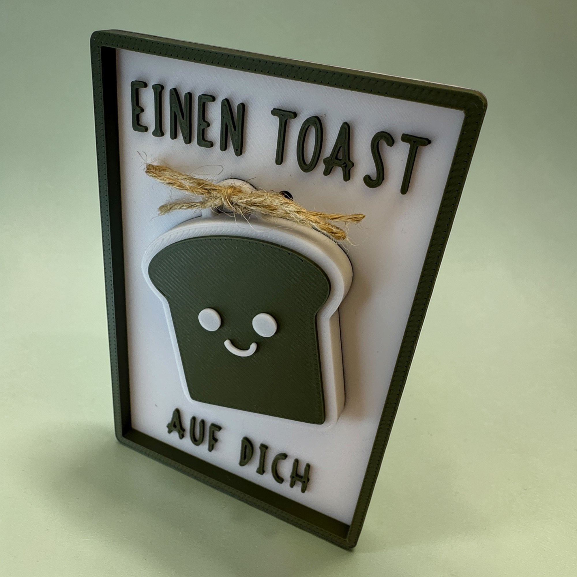 Leicht seitlich präsentierte Glückwunschkarte mit Toast-Schlüsselanhänger und Spruch Einen Toast auf dich in Olivgrün.
