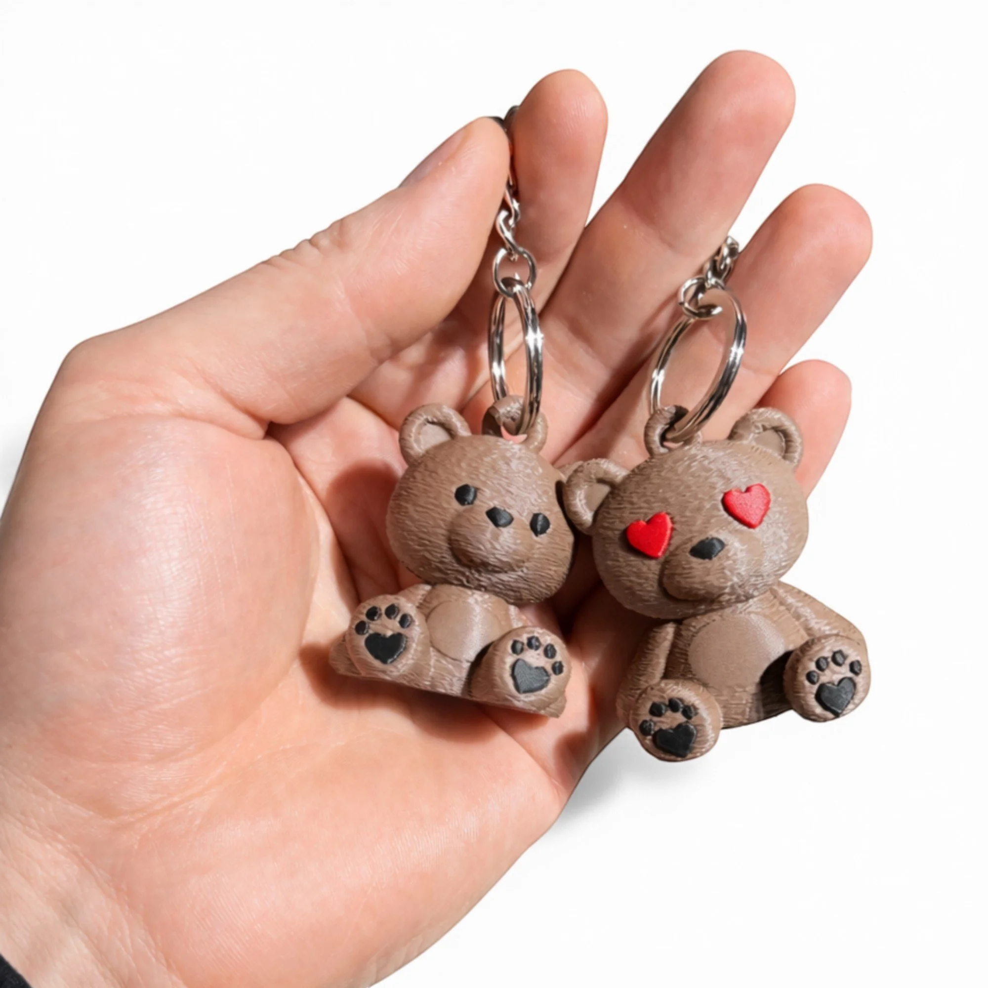 Zwei Teddy Schlüsselanhänger in einer Hand, eine Variante mit Herzaugen und eine mit klassischen Augen, als passendes Duo für Schlüsselbund oder Tasche.