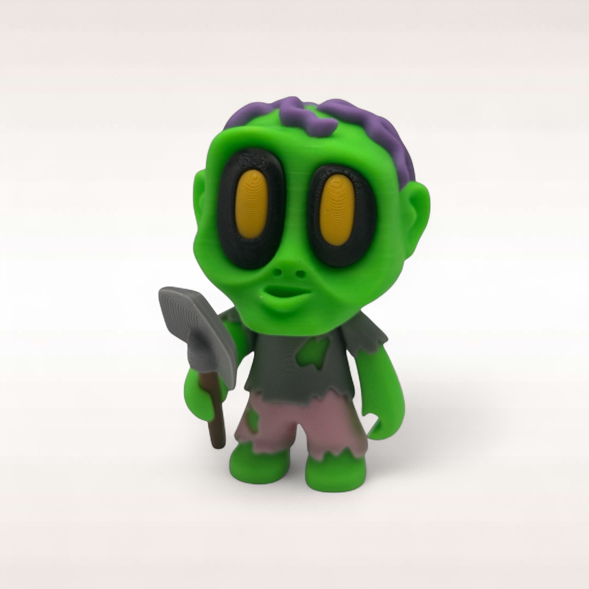 Grüner Mini-Zombie mit Schaufel, großen Augen und lilafarbenen Details freigestellt auf weißem Hintergrund.