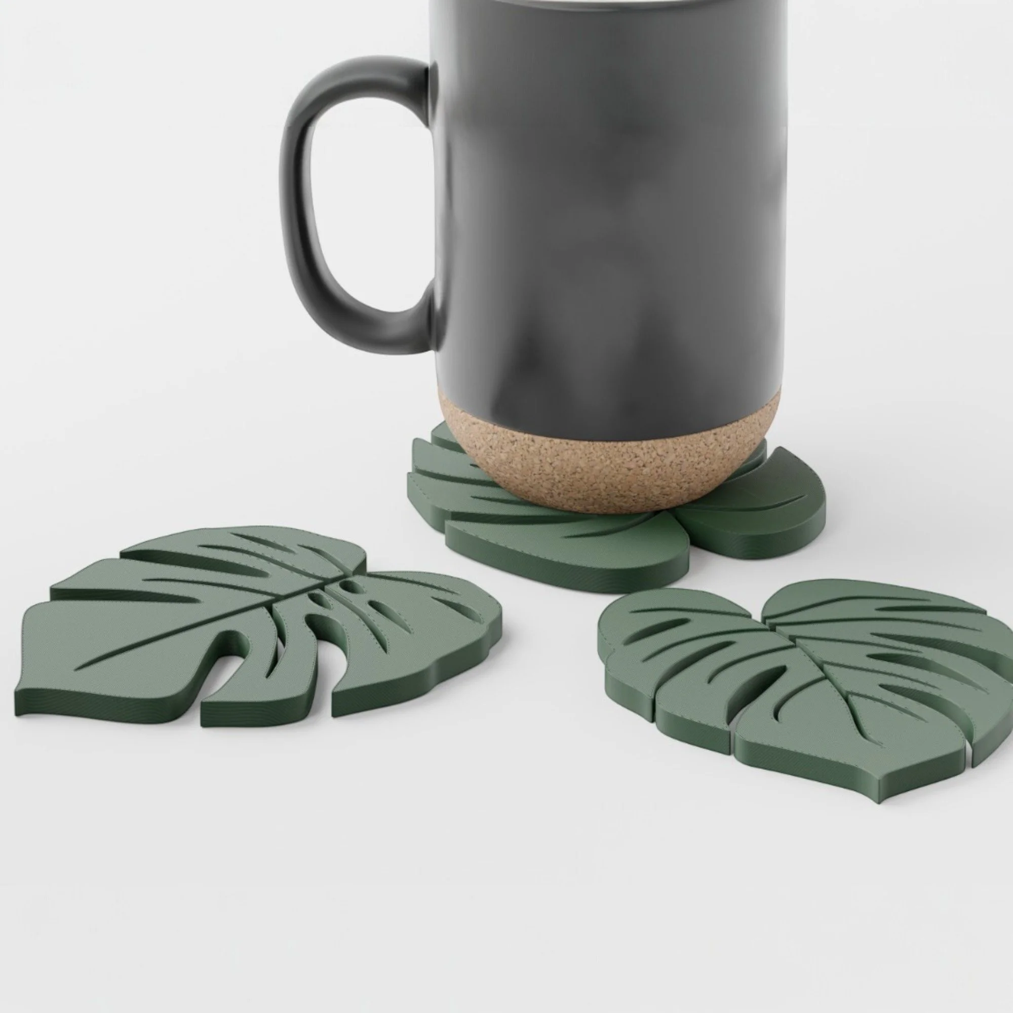 Nahaufnahme einer schwarzen Tasse auf grünem Monstera-Untersetzer mit zwei weiteren Blatt-Untersetzern daneben