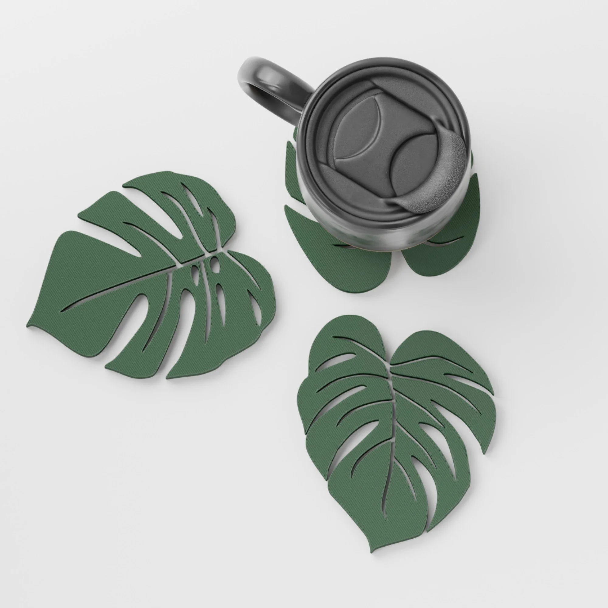 Drei Monstera-Untersetzer im Set aus der Vogelperspektive, kombiniert mit einer schwarzen Tasse und drei unterschiedlichen grünen Blattformen