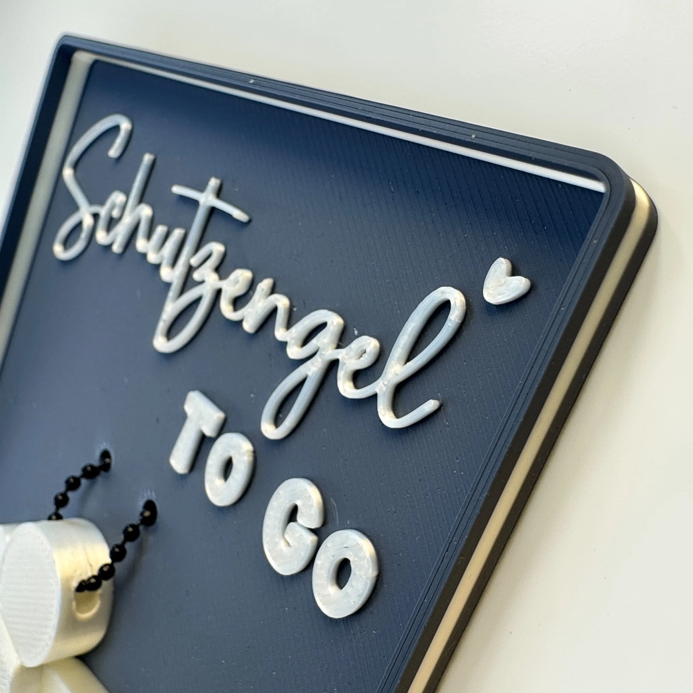 Dunkelblaue Spruchschale mit Schutzengel to go aus schräger Perspektive, mit weißem Engel Anhänger und kleinem Herz als liebevolle Aufmerksamkeit.