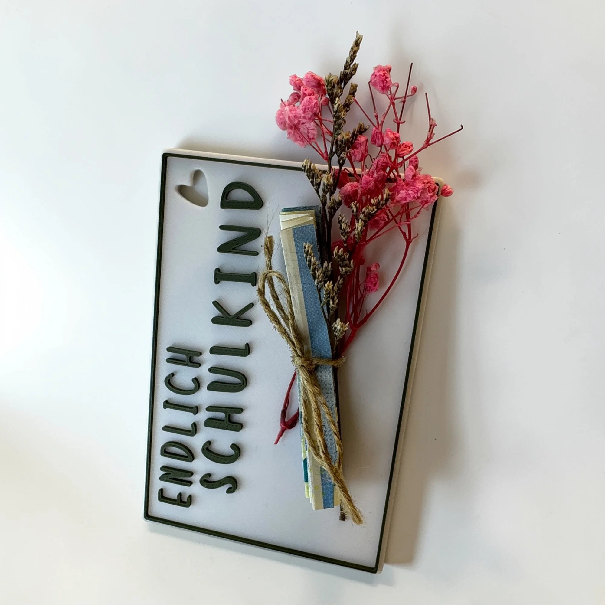 Weiße Geschenkkarte zur Einschulung mit Schriftzug Endlich Schulkind und kleinem rosa Blütenstrauß, schräg vor hellem Hintergrund aufgestellt.