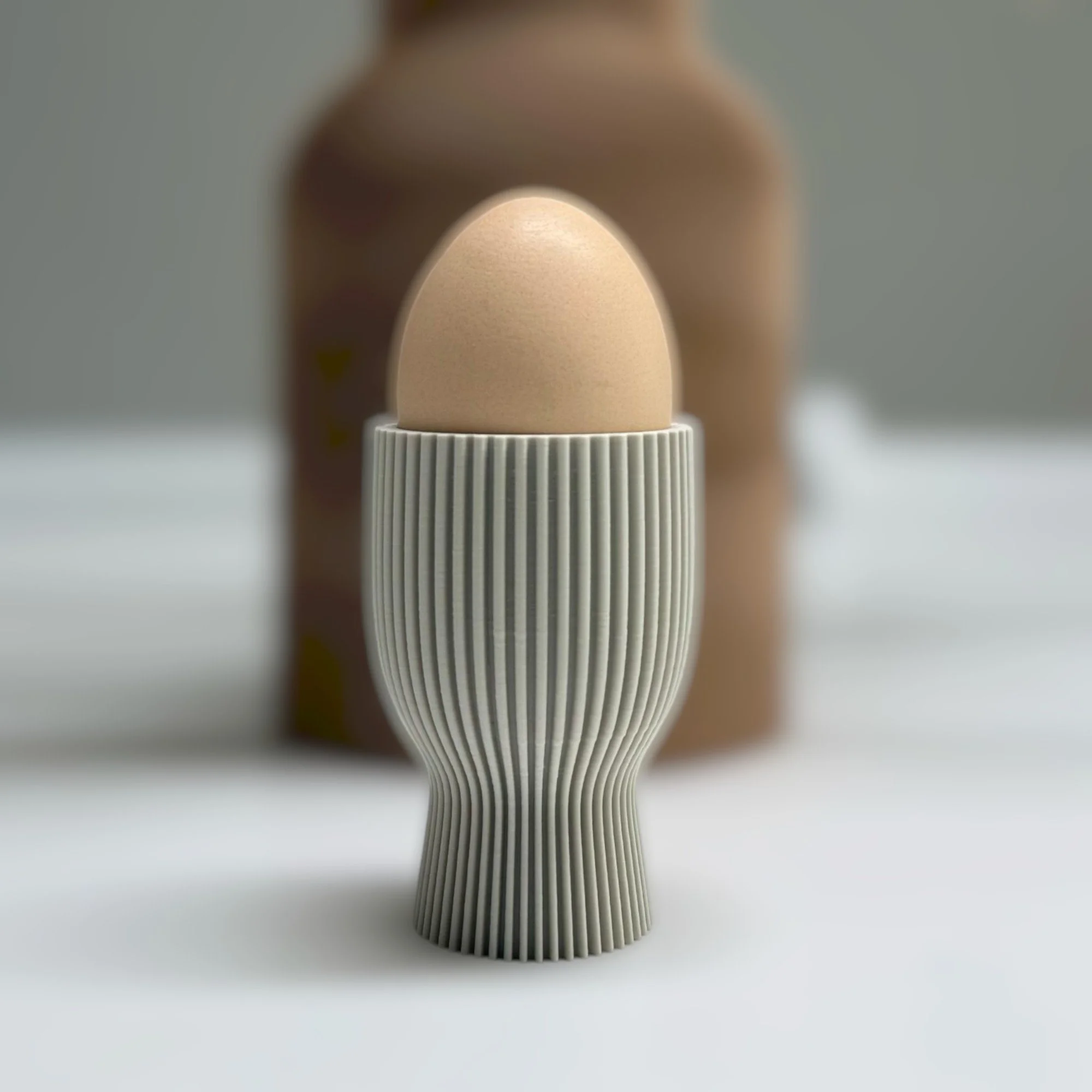 Wendbarer Eierbecher in heller Farbe mit Ei, minimalistisch gestaltet und erhöht geformt für Osterfrühstück, Brunch und stilvolle Tischdeko.