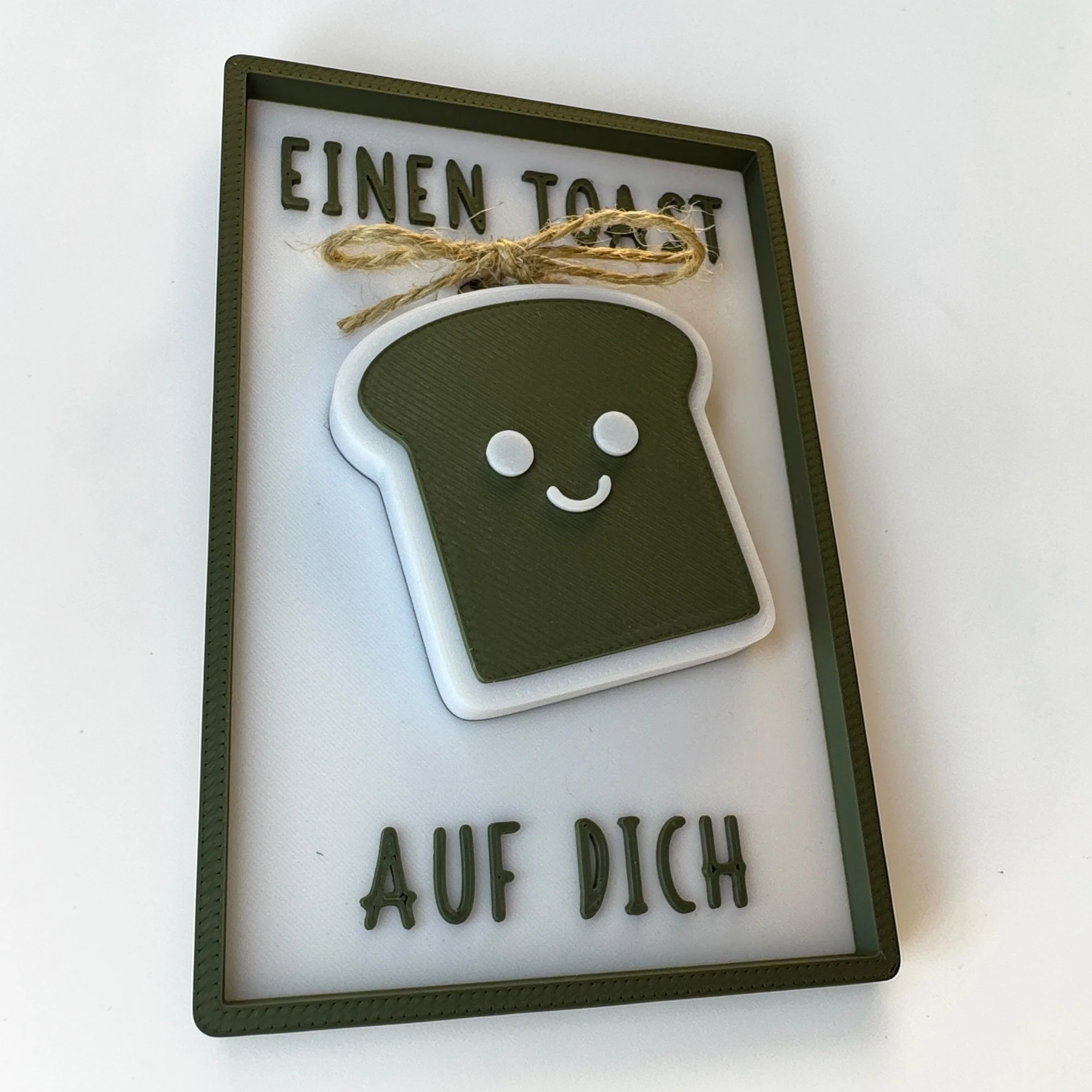 Einzugskarte mit befestigtem Toast-Schlüsselanhänger und Schriftzug Einen Toast auf dich, leicht schräg fotografiert.