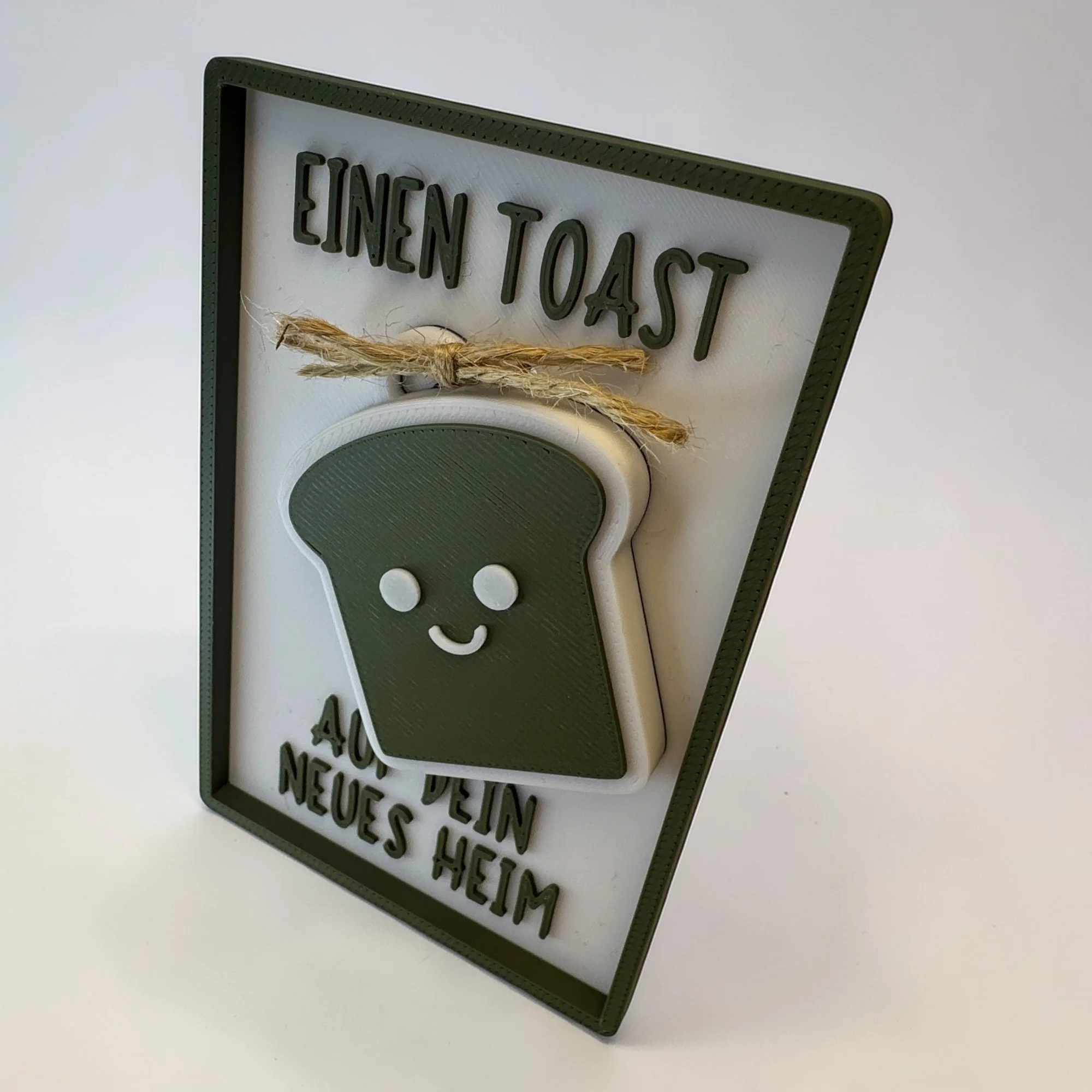 Seitlich aufgestellte Karte mit olivgrünem Toast-Schlüsselanhänger und Spruch Einen Toast auf dich vor hellem Hintergrund.