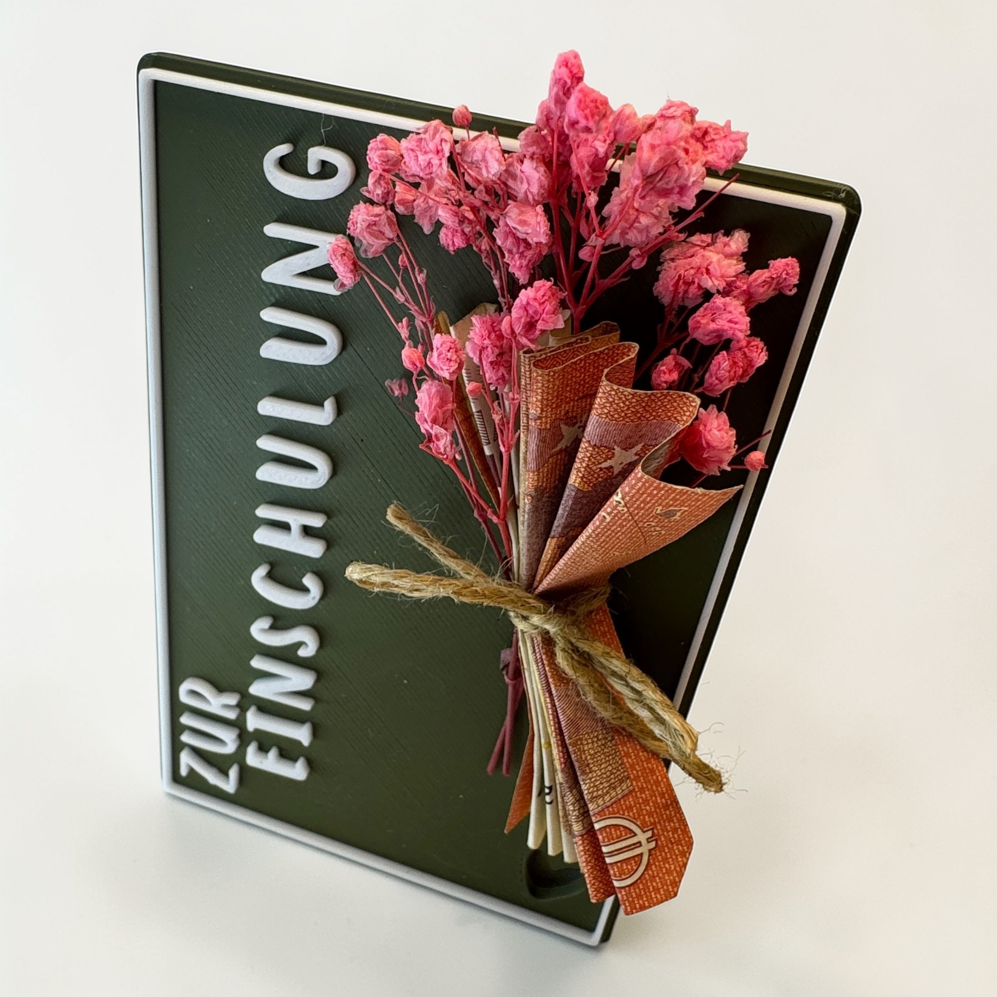 Nahaufnahme der dunkelgrünen Geschenkkarte Zur Einschulung mit weißer Schrift, Kordel und kleinem Strauß in Rosa und Naturtönen.