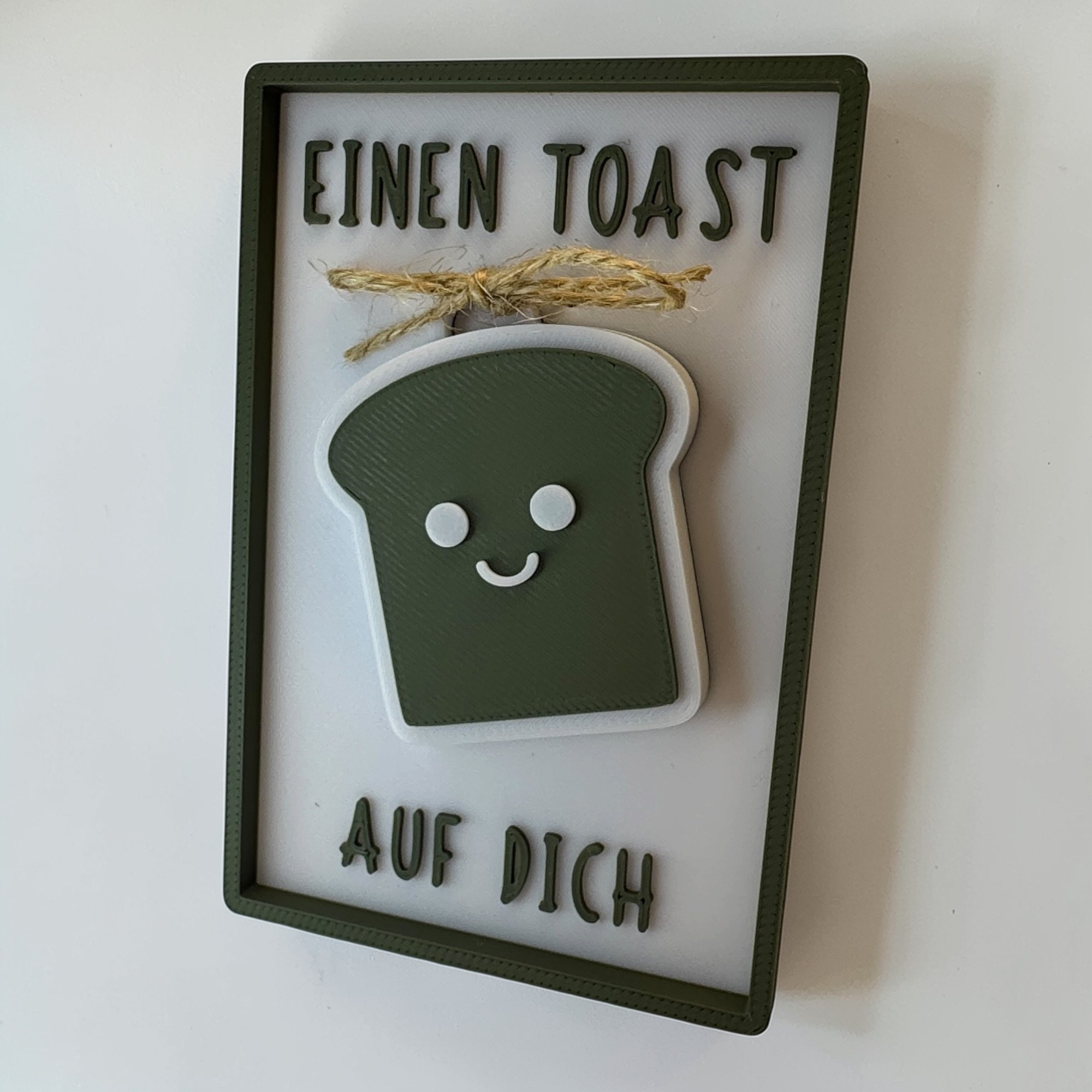Frontal gezeigte Glückwunschkarte in Weiß und Olivgrün mit Toast-Schlüsselanhänger und Spruch Einen Toast auf dich.