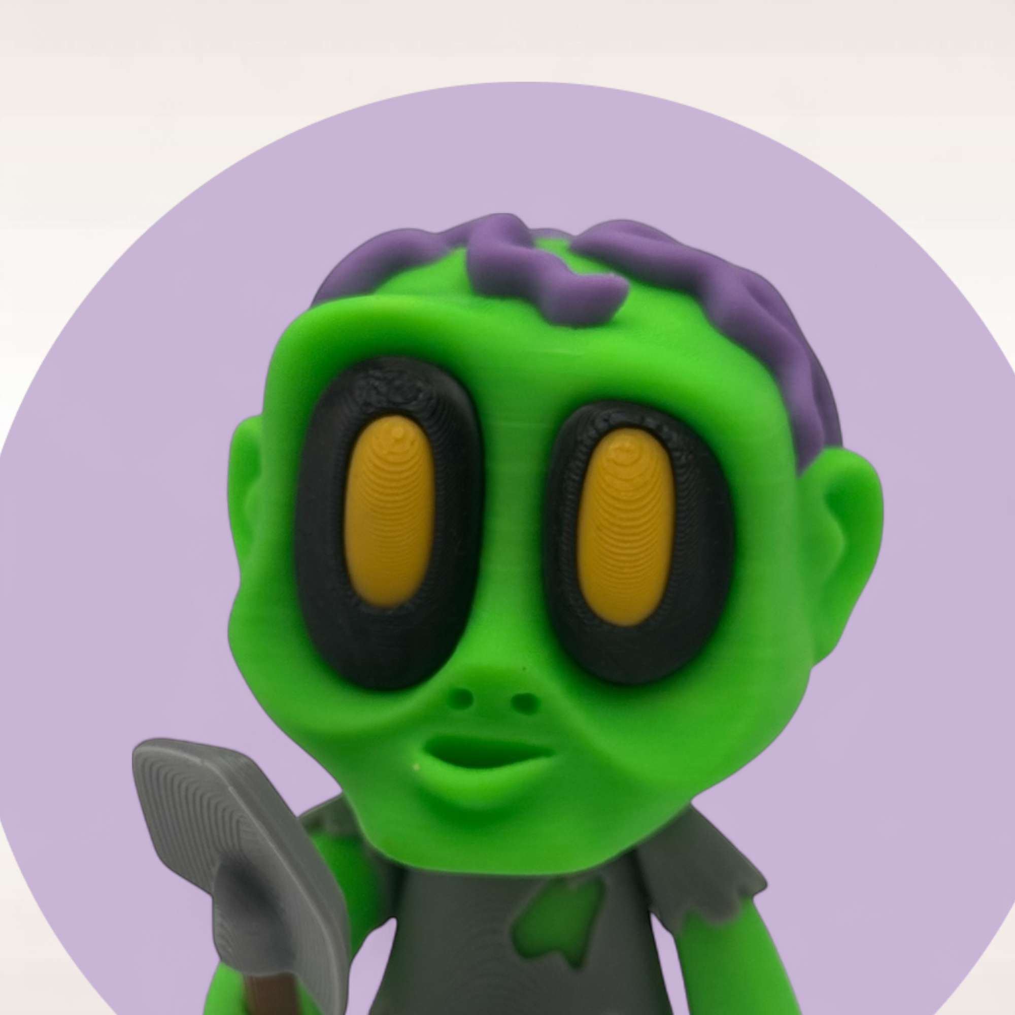 Nahaufnahme eines grünen Mini-Zombies mit gelb-schwarzen Augen, lilafarbenen Details und kleiner Schaufel als detailreiche 3D-Druck-Figur.