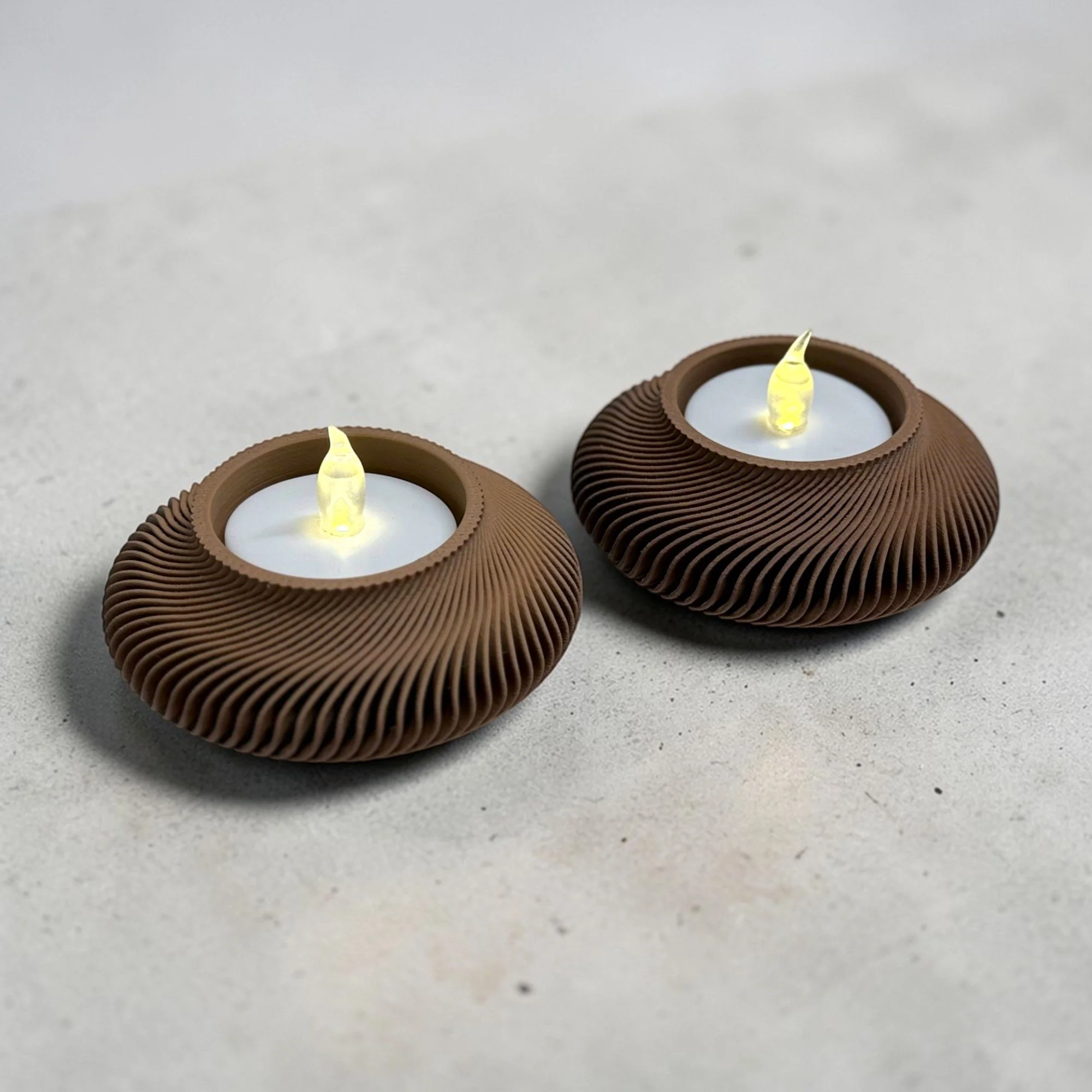 Zwei gerippte LED-Teelichthalter in Dunkelbraun auf grauem Untergrund mit sanfter Lichtwirkung als elegante Deko zum chinesischen Neujahr.