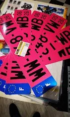 Paquets de bracelets de course colorés, principalement en rose, violet et bleu, avec des inscriptions telles que 'WBB' et '0.4 km', empilés sur une surface.