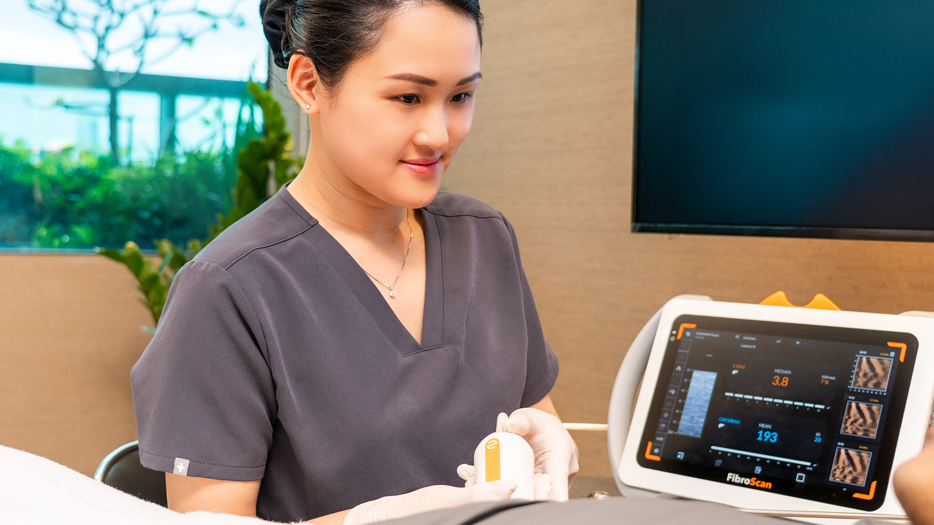 R17 female wellness longveity professional wearing gray scrubs and gloves operating a FibroScan device in a clinical setting.