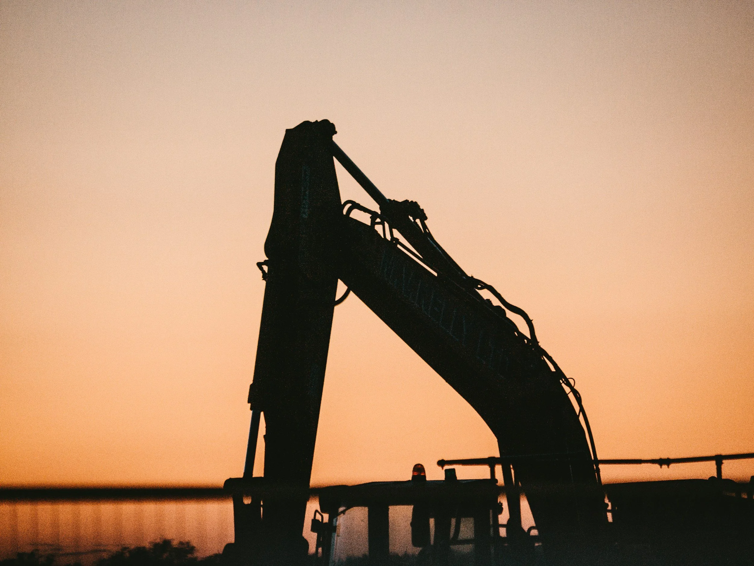 Silhouette of an excavator against a sunset sky.