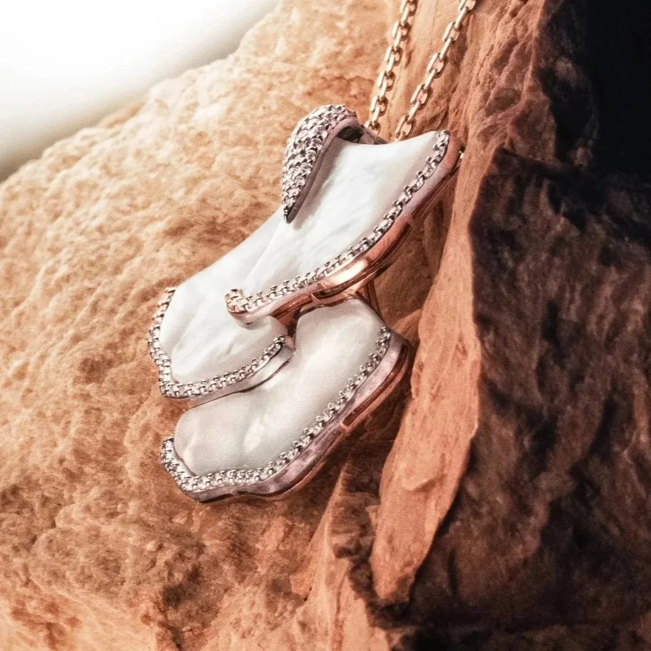 Collier élégant avec une chaîne en métal, un pendentif en forme de chaussure en nacre entourée de petites pierres brillantes, posé sur une roche, photo en gros plan.