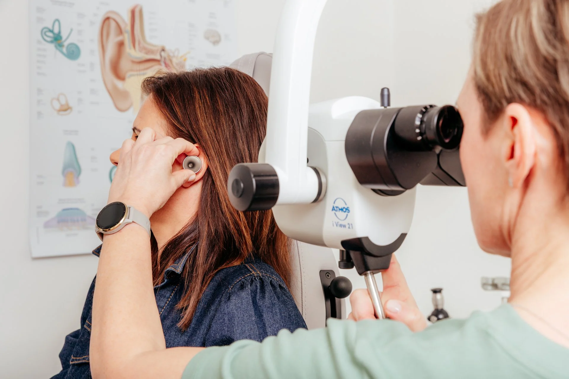 Ärztin bei Ohrenuntersuchung mit einem Otoskop bei einer Patientin in einer Arztpraxis, Erklärung im medizinischen Umfeld