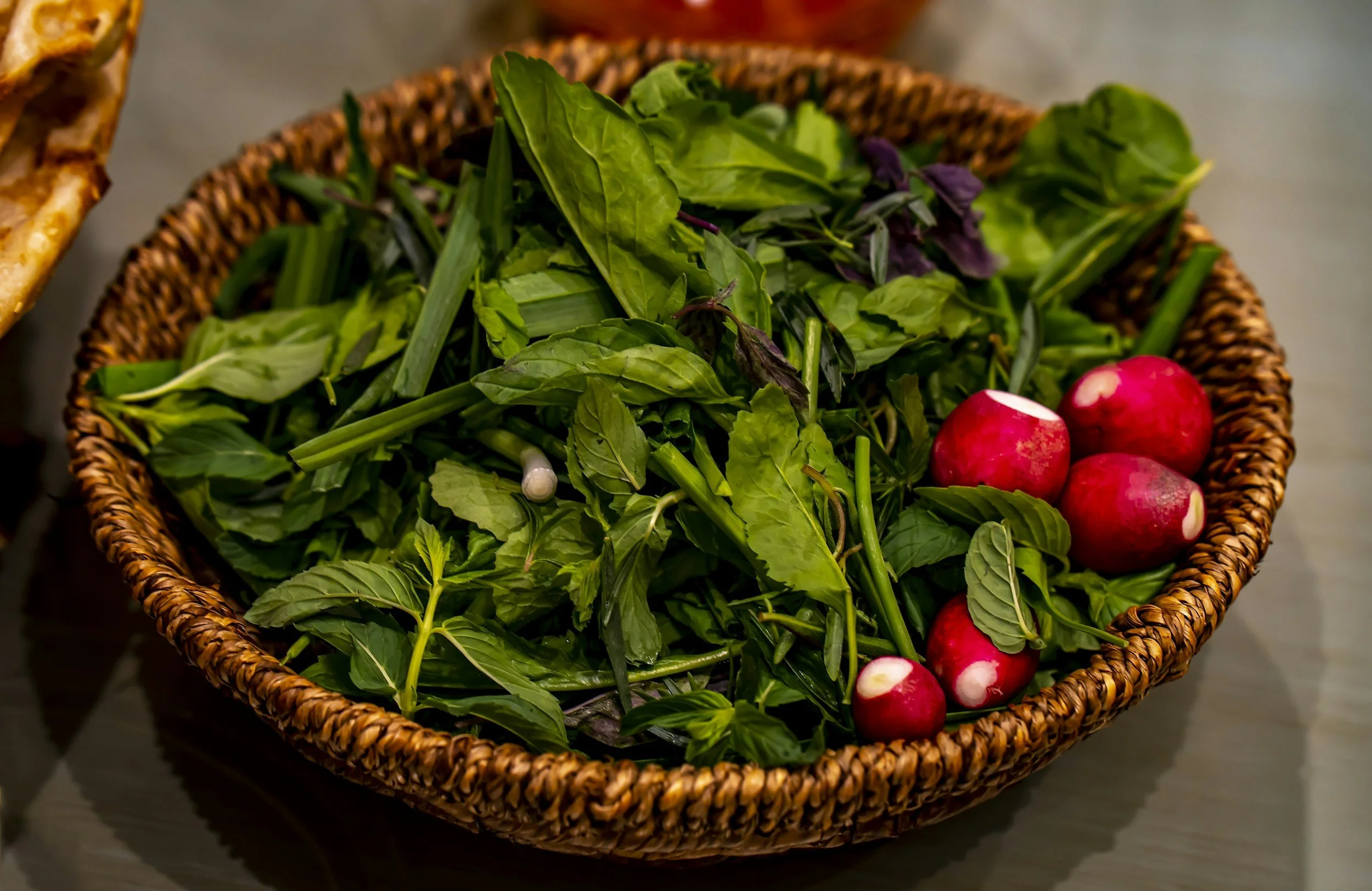 A woven basket filled with fresh green herbs and radishes.